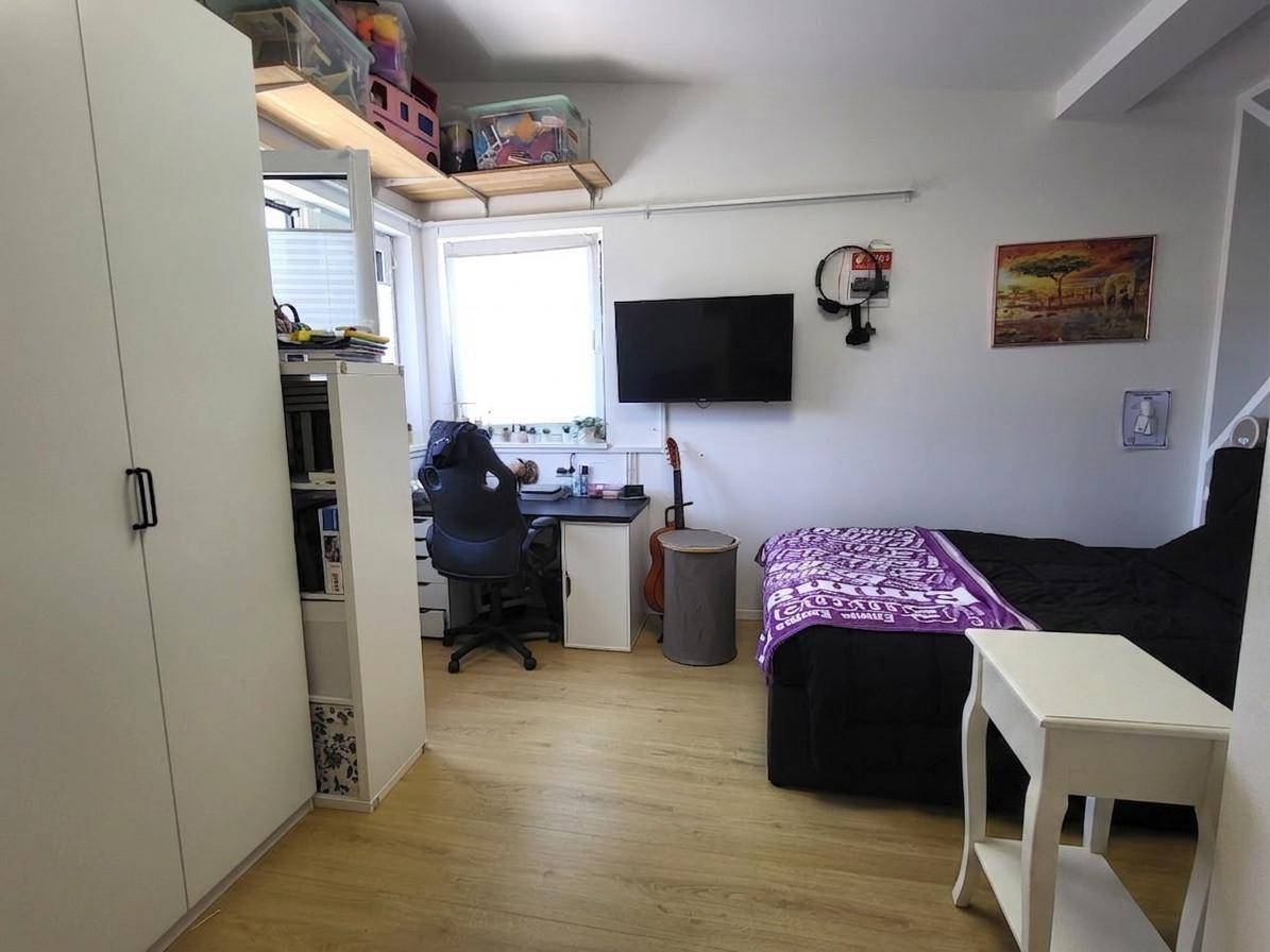 Helles Schlafzimmer mit Schreibtisch, Bett und Blick aus dem Fenster.