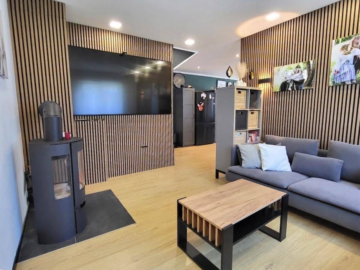 Modernes Wohnzimmer mit Holzwandverkleidung, Kaminofen und bequemer Couch.