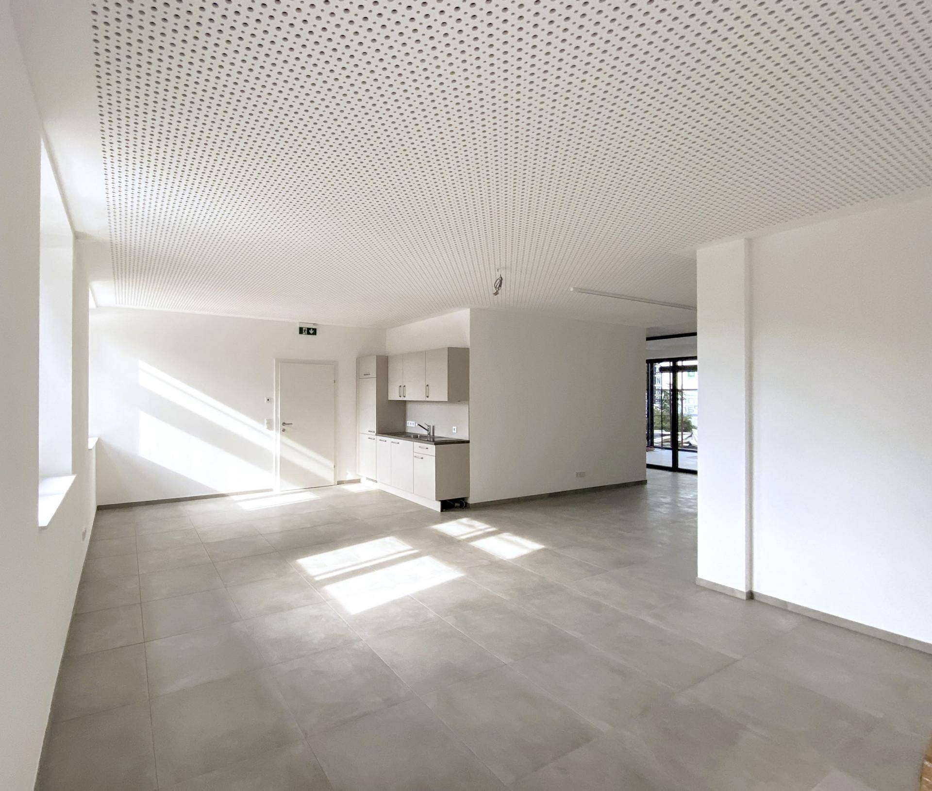 Geräumiger, lichtdurchfluteter Gewerberaum mit minimalistischer Küchenzeile, großen Fenstern und modernen Fliesenboden.