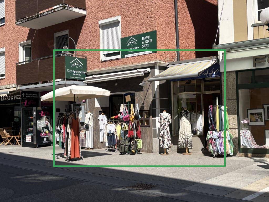 Geschäftsfassade mit Schaufenstern und Outdoor-Kleiderständern an einer belebten Straße.