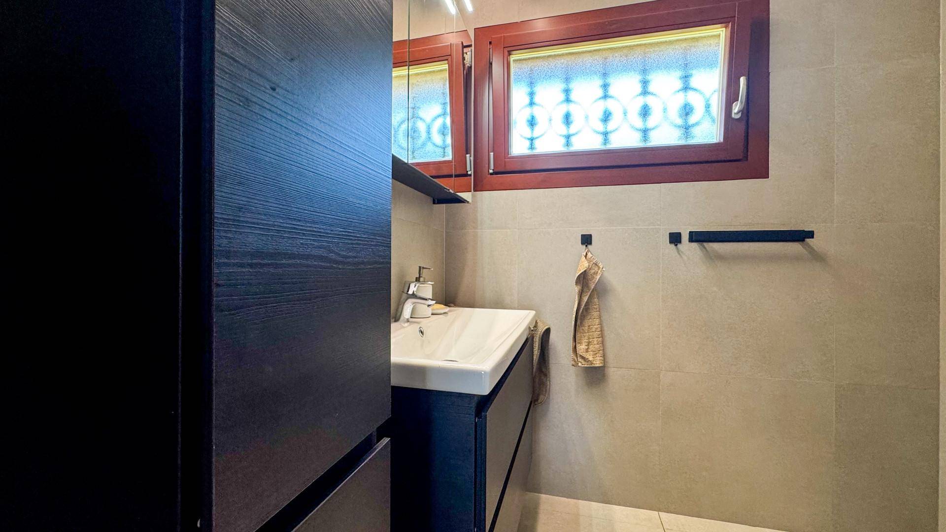 Badezimmer mit modernem Waschbecken, dunklen Möbeln und Fenster mit Musterglas.