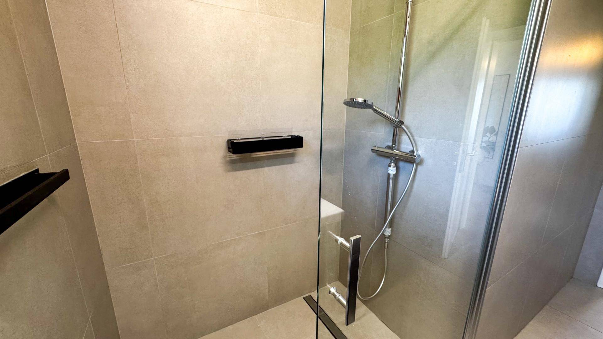Moderne Dusche mit Glasabtrennung und hellgrauen Fliesen im Badezimmer.