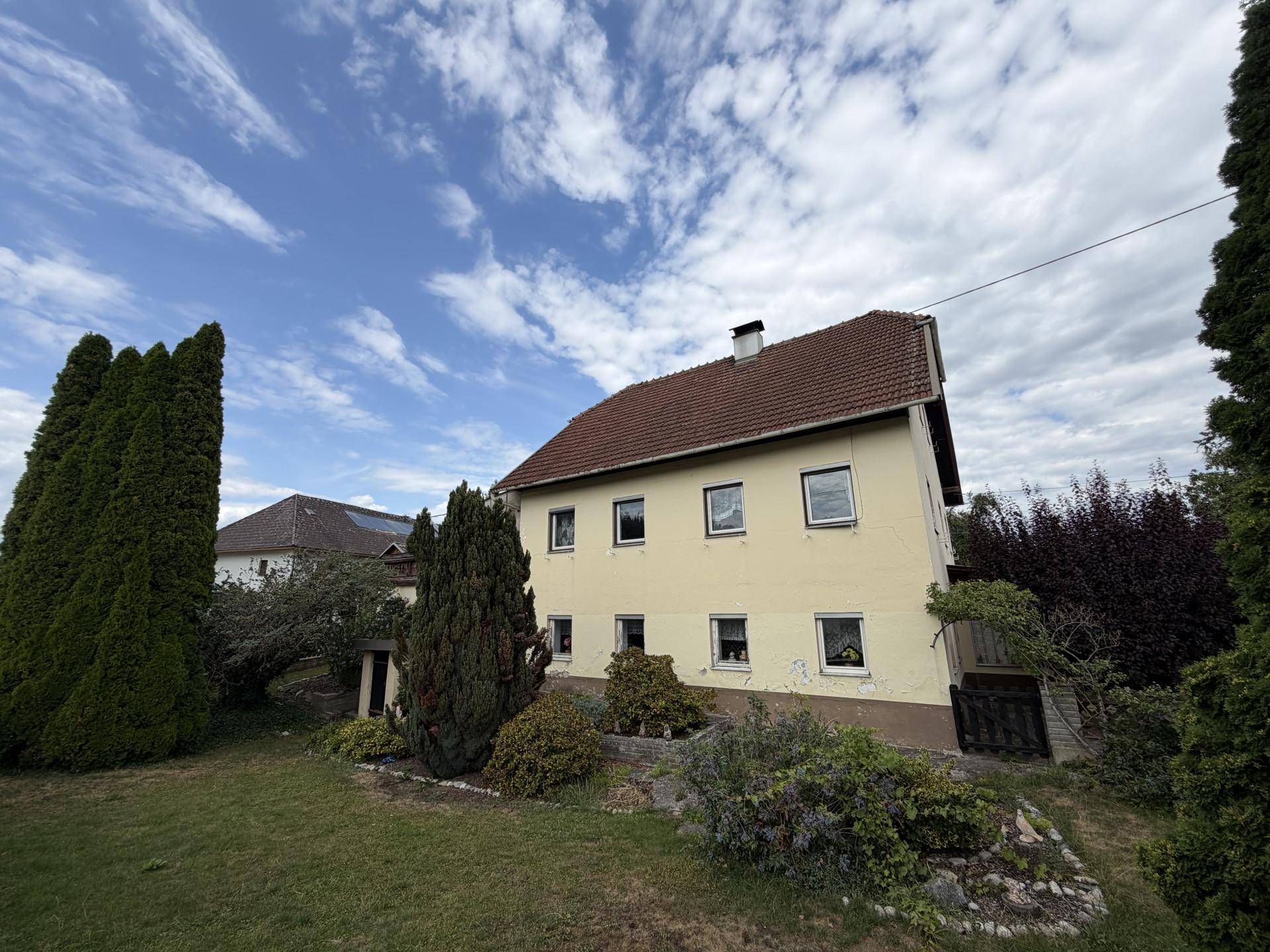 Rückansicht des Wohnhauses mit Gartenbereich und hohen Bäumen unter blauem Himmel.