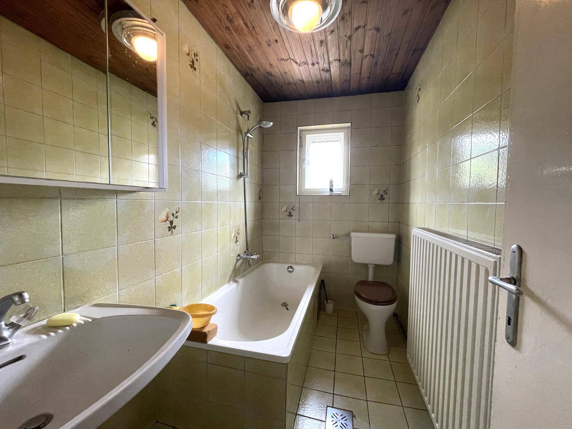 Badezimmer mit hellgrünen Fliesen, Badewanne mit Duschfunktion und Holzdecke.