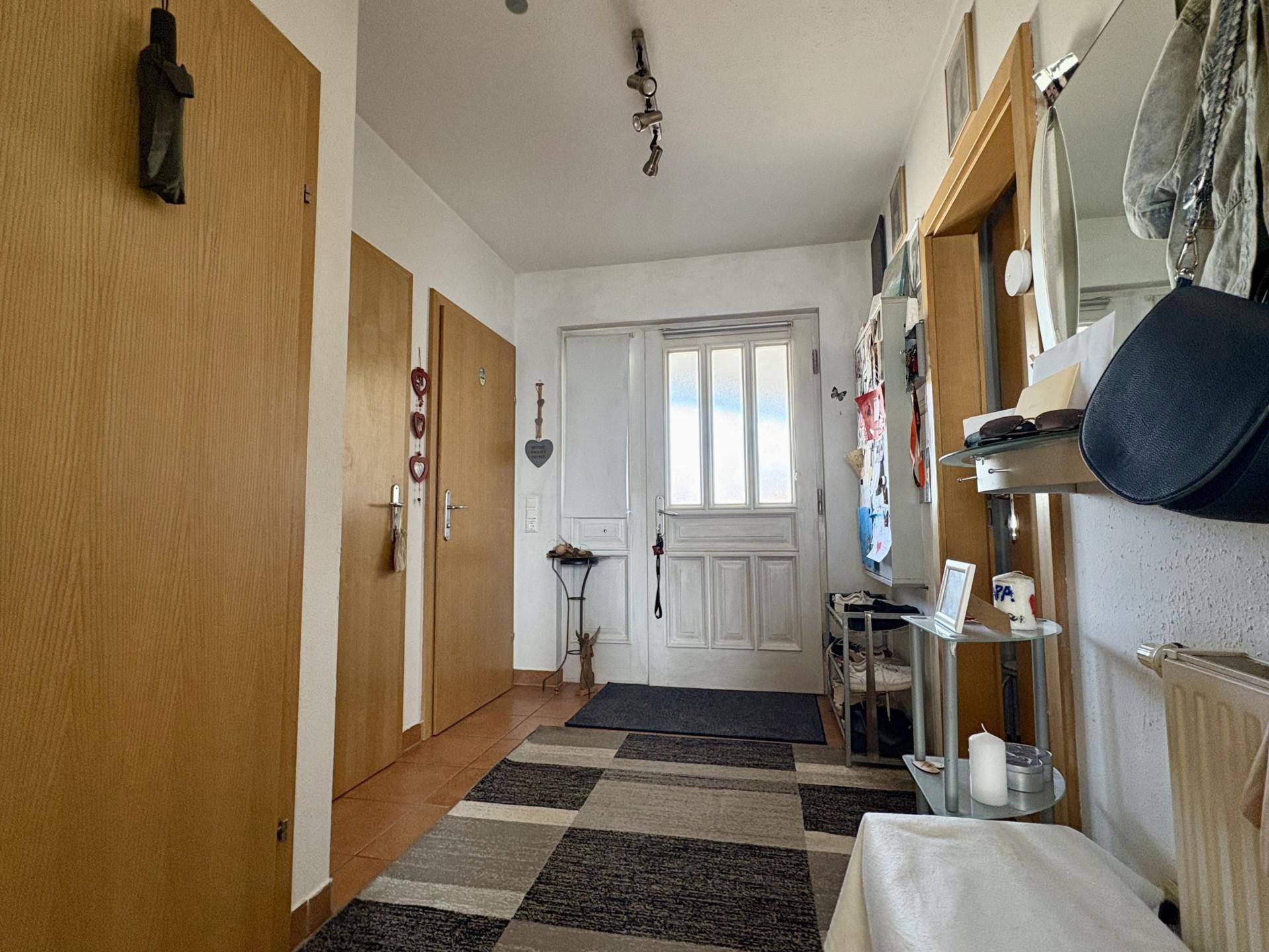 Heller Eingangsbereich mit Fliesenboden, Holztüren und viel Tageslicht durch die Haustür.