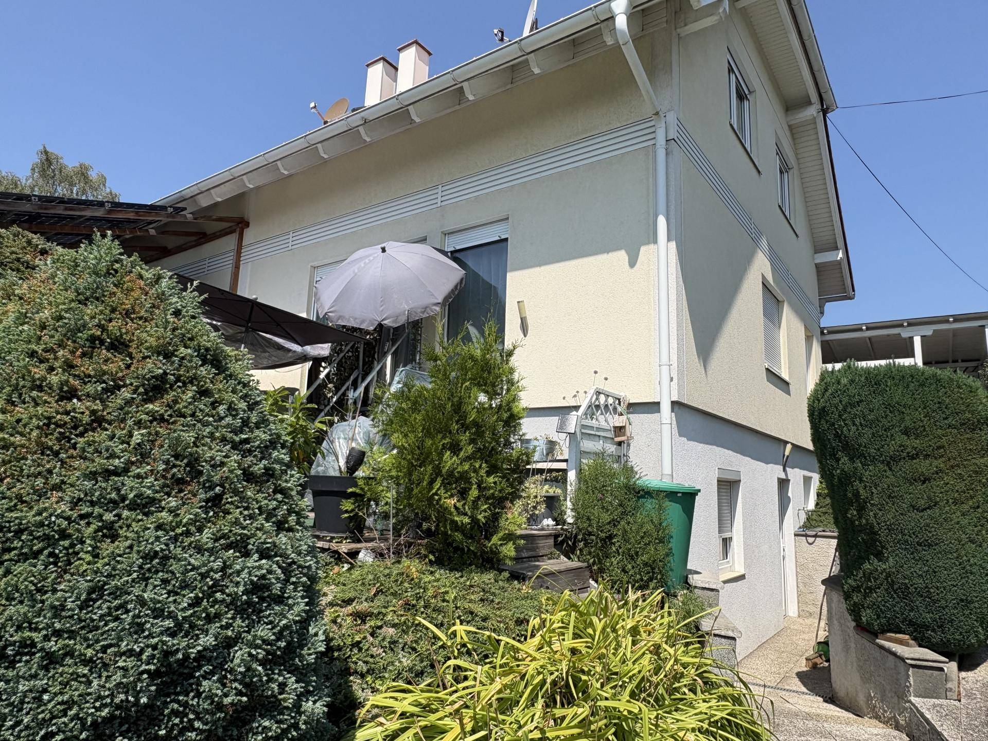 Seitenansicht des Hauses mit Gartenbereich, Treppe und üppiger Bepflanzung.