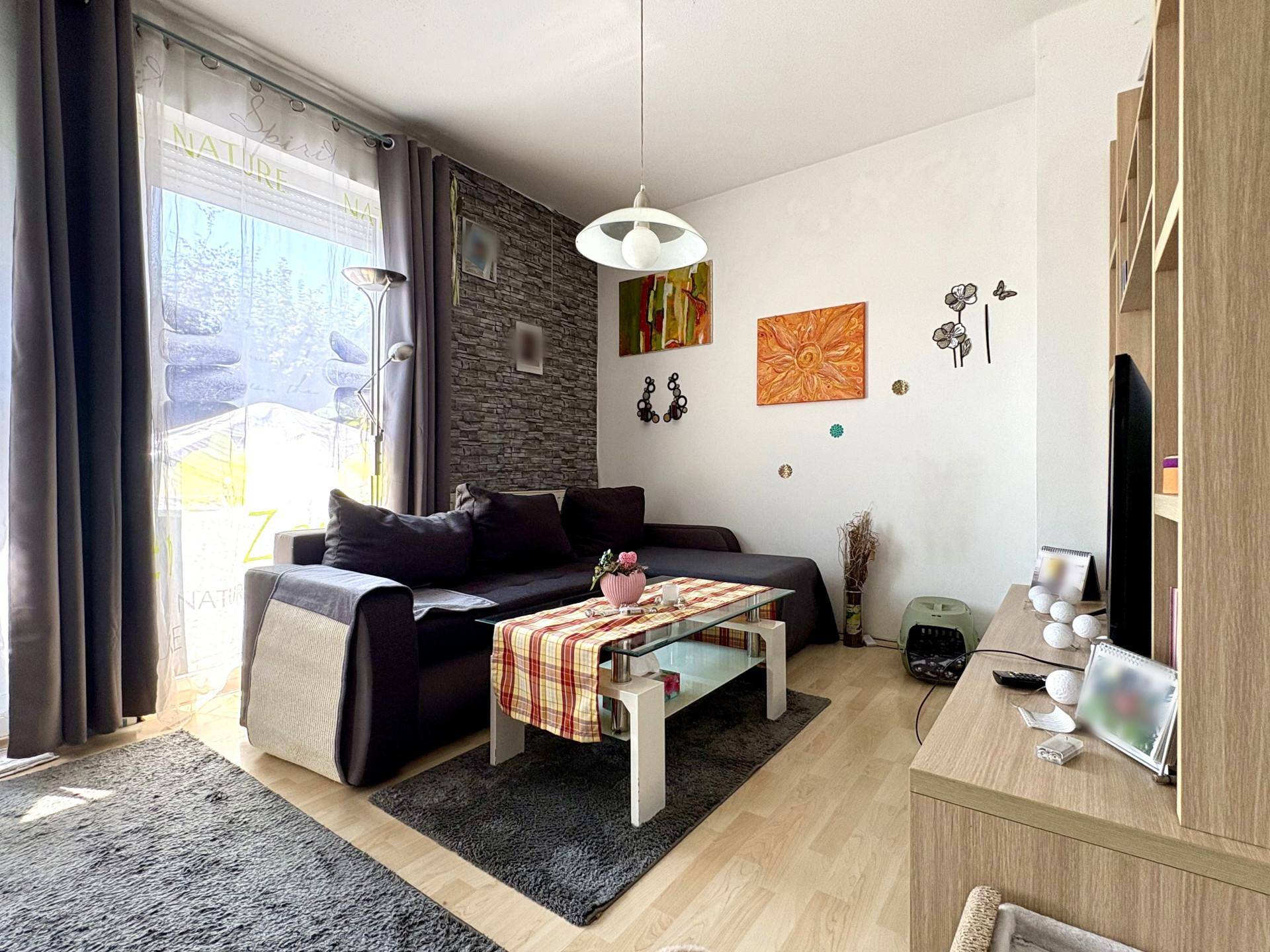 Gemütliches Wohnzimmer mit dunklem Sofa, Teppichboden und großem Fenster für viel Licht.
