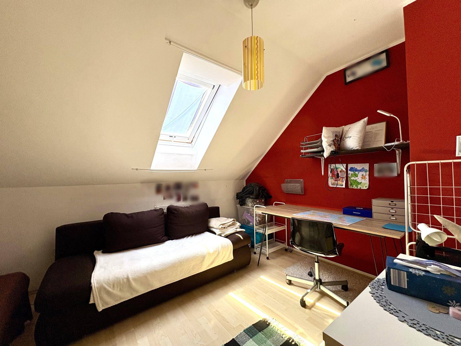 Helles Arbeitszimmer im Dachgeschoss mit Schreibtisch, Sofa und Dachfenster.
