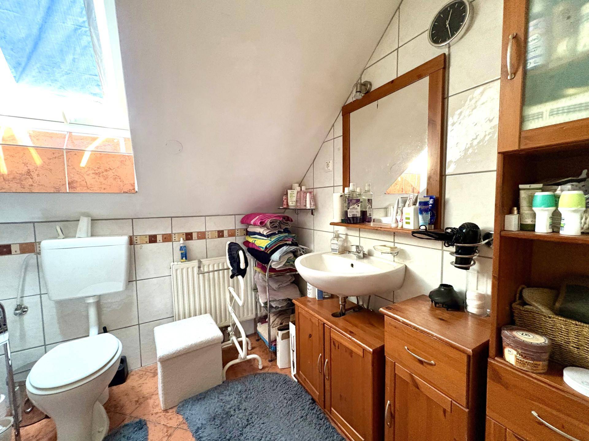 Badezimmer im Dachgeschoss mit WC, Waschbecken, Holzschränken und Dachfenster.