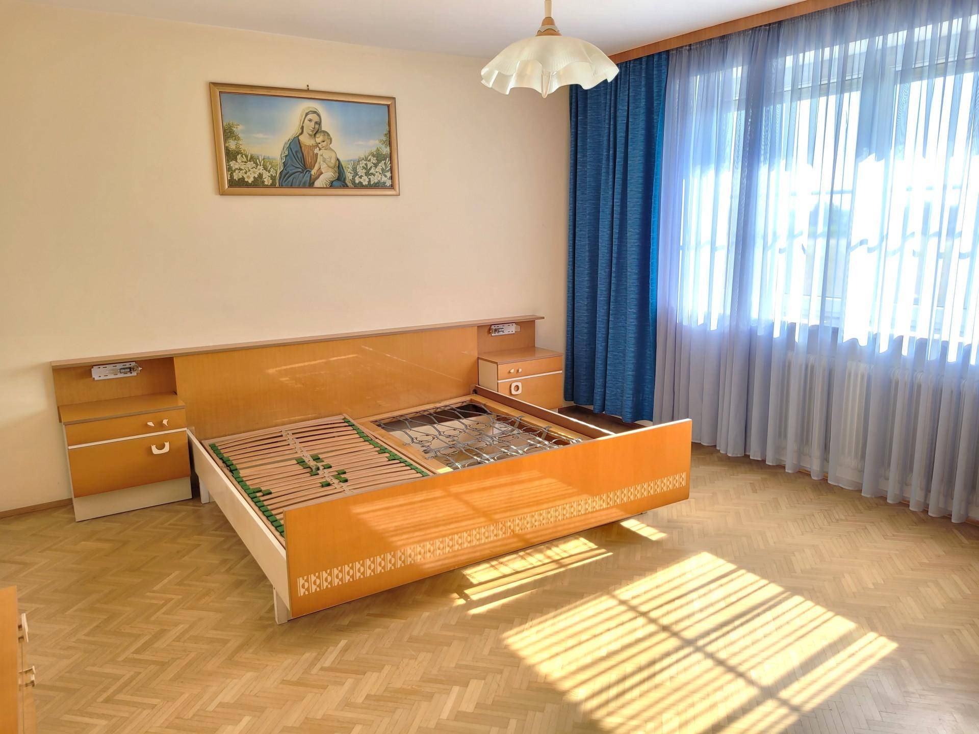 Schlafzimmer mit Parkettboden, großem Fenster und traditioneller Einrichtung.