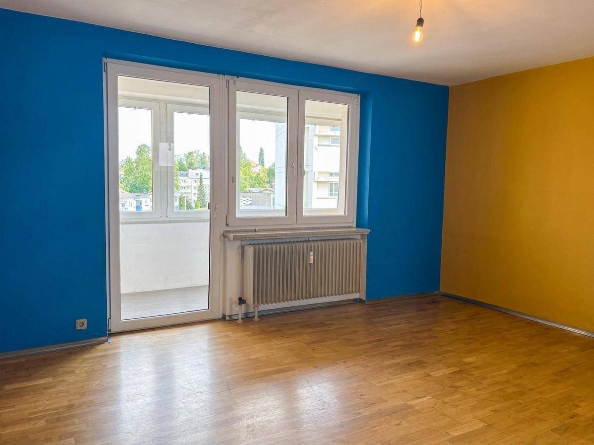 Heller Raum mit Holzboden, blauen und gelben Wänden sowie Zugang zu einem Balkon.