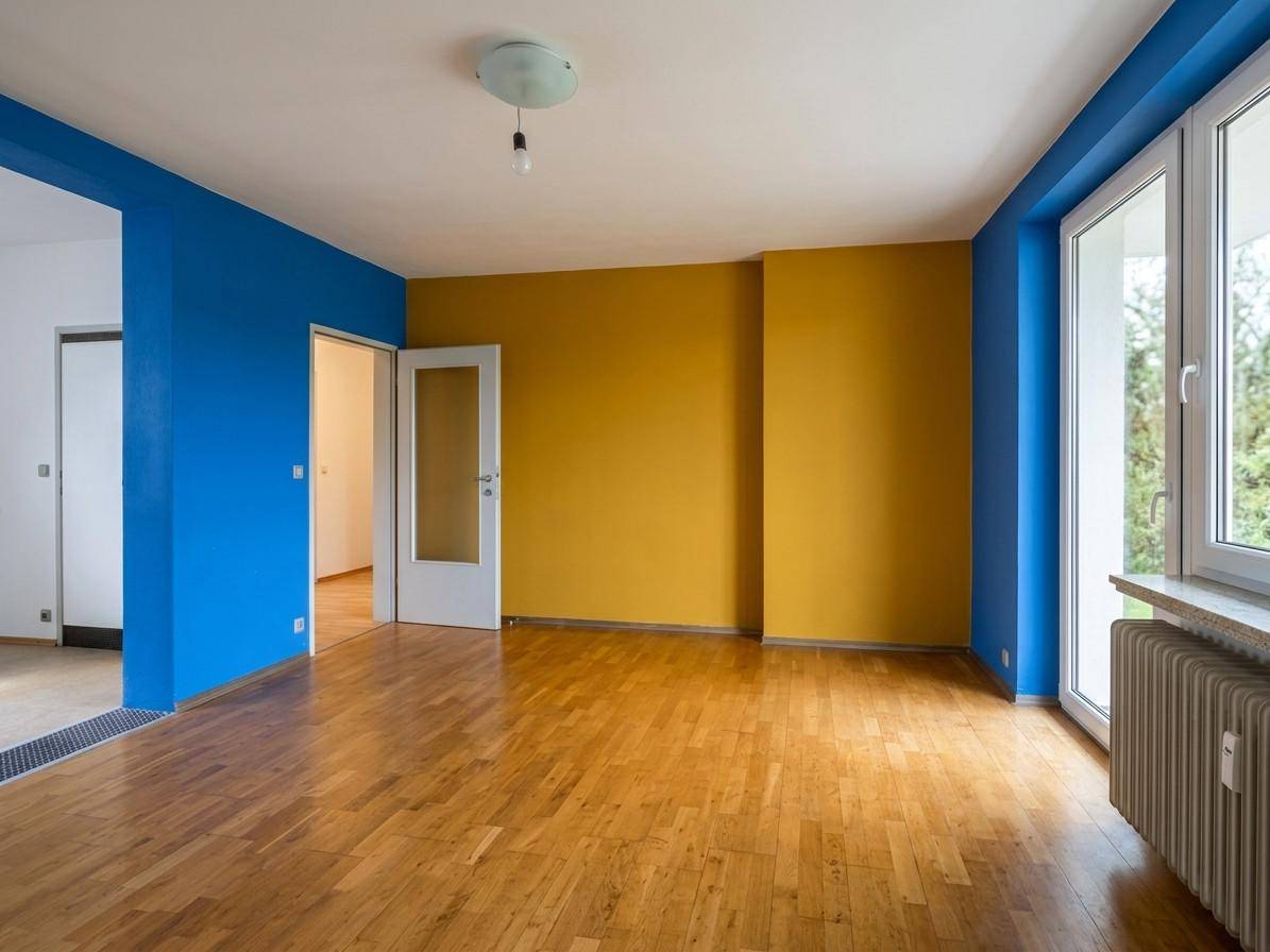 Geräumiger Wohnbereich mit Holzboden, farbigen Wänden und großen Fenstern für viel Licht.