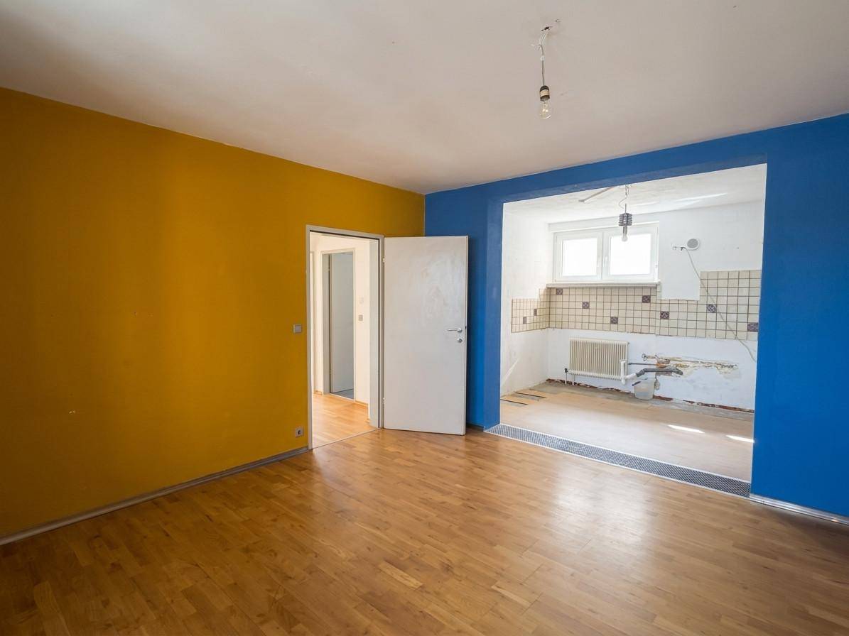 Leerer Küchenbereich mit Fliesen an der Wand, blauen und gelben Wänden und Holzboden.