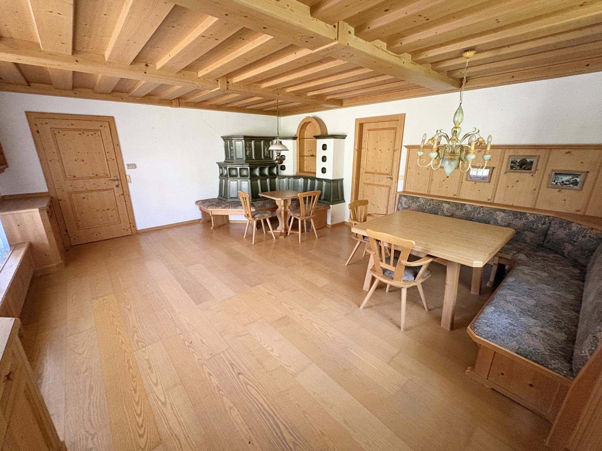 Gemütlicher Wohn-Essbereich im alpinen Stil mit Holzbalkendecke, Parkettboden und traditionellem Kachelofen.