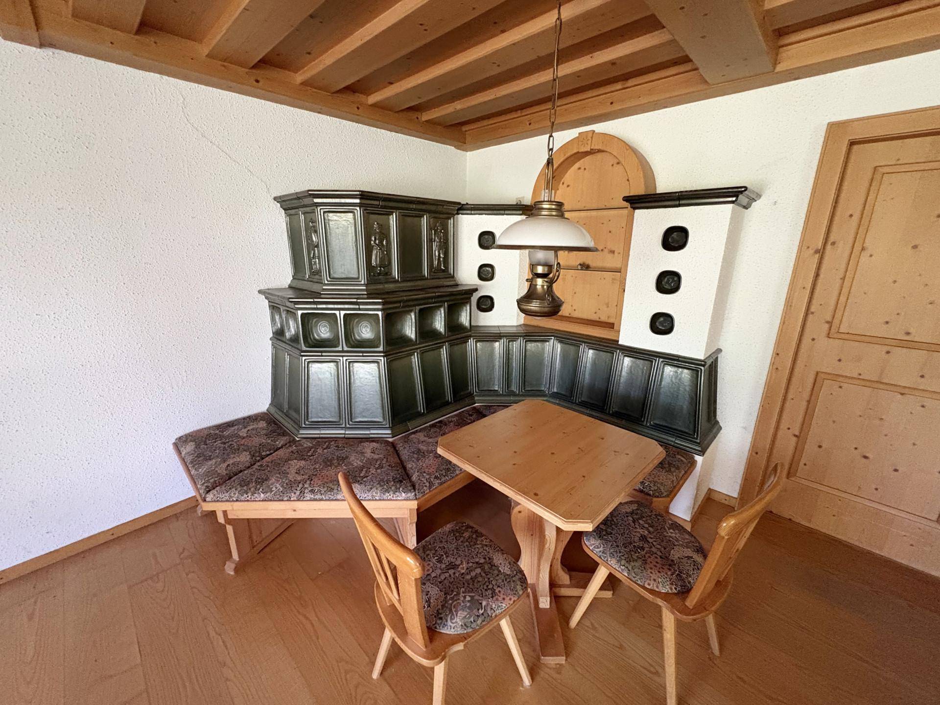 Detailansicht des traditionellen grünen Kachelofens mit Sitzbank und einem kleinen Esstisch im alpinen Stil.