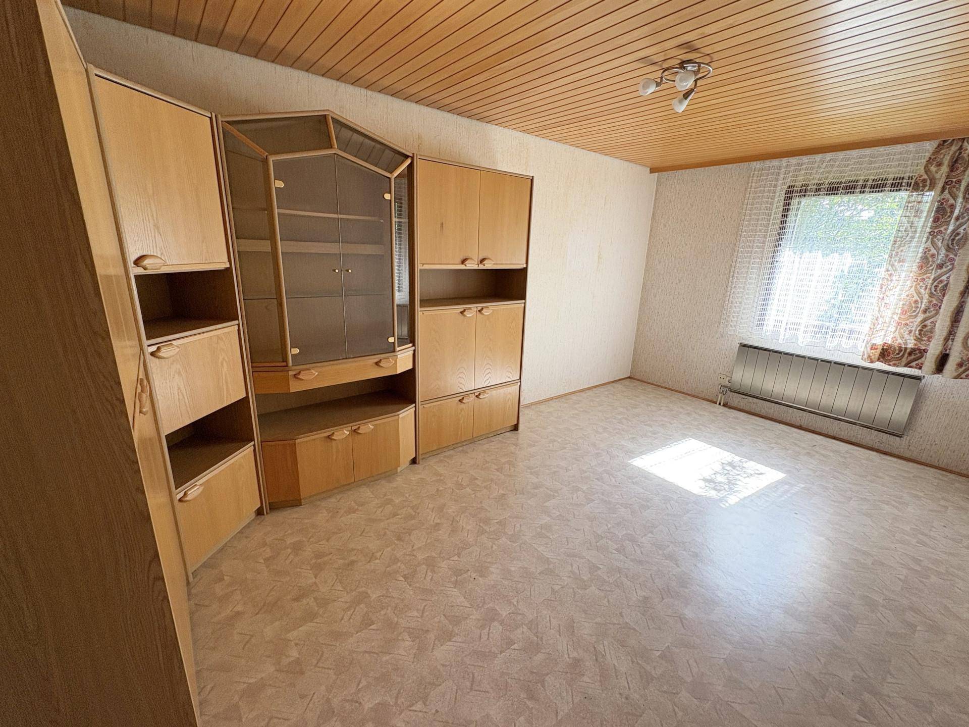 Geräumiges Zimmer mit großem Holzschrank, Laminatboden und einem Fenster mit Blick ins Grüne.