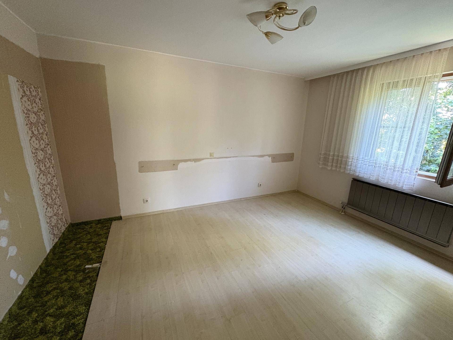 Helles, leeres Zimmer mit hellem Bodenbelag und einem Fenster, das viel Tageslicht hereinlässt.