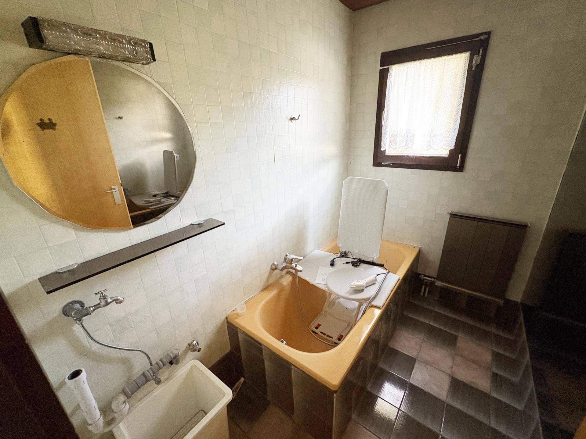 Badezimmer im 80er-Jahre-Stil mit gelber Badewanne, Fliesen und einem Fenster für Tageslicht.