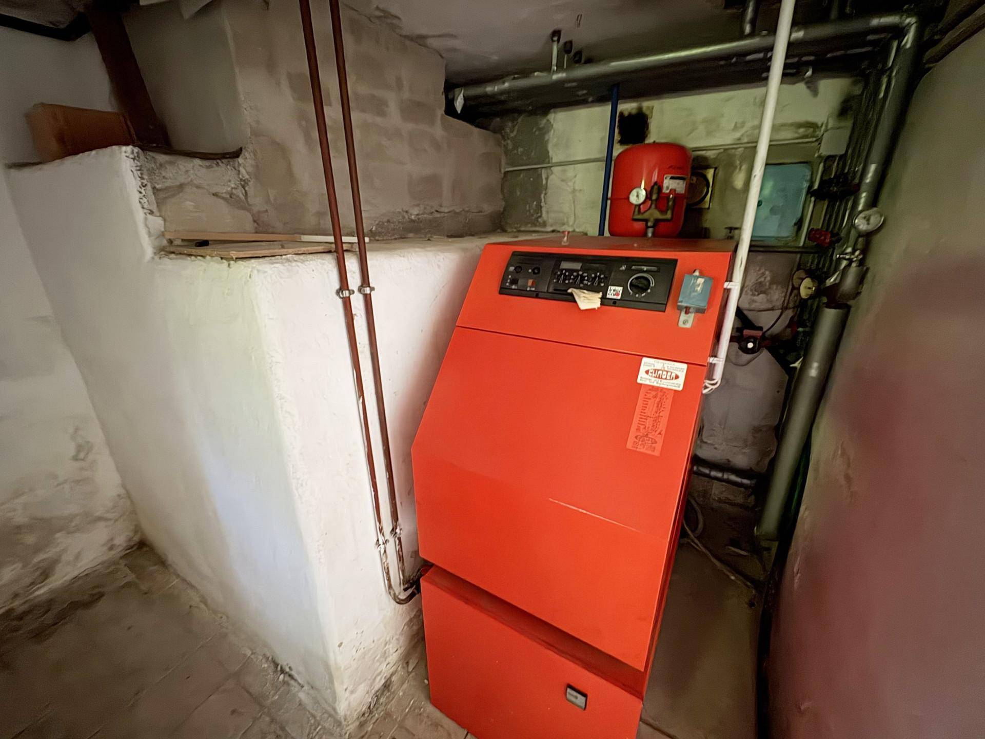 Heizungsraum im Keller mit einem großen, roten Heizkessel und sichtbaren Rohrleitungen.