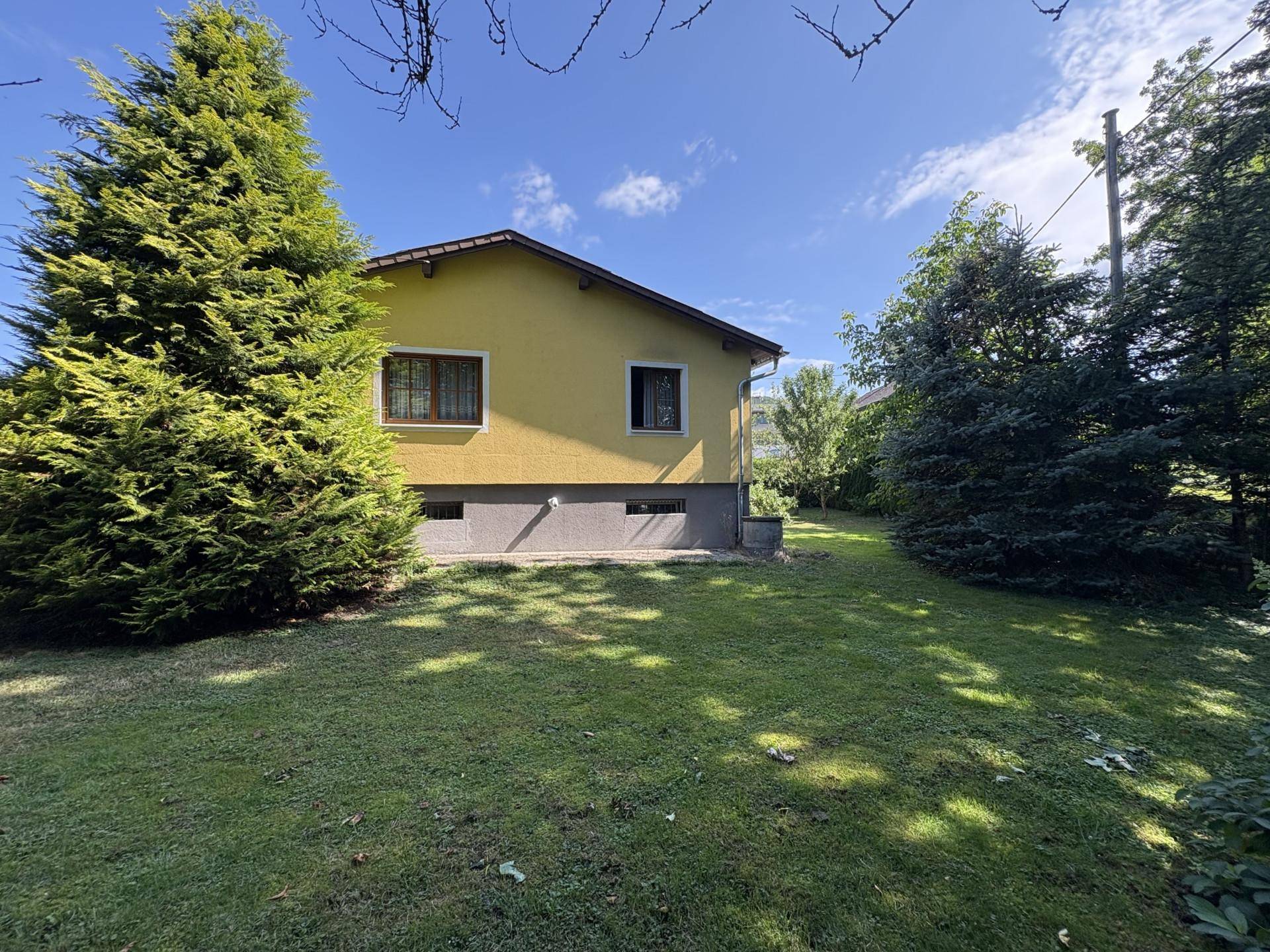 Weitere Seitenansicht des gelben Einfamilienhauses mit großem Garten und altem Baumbestand.