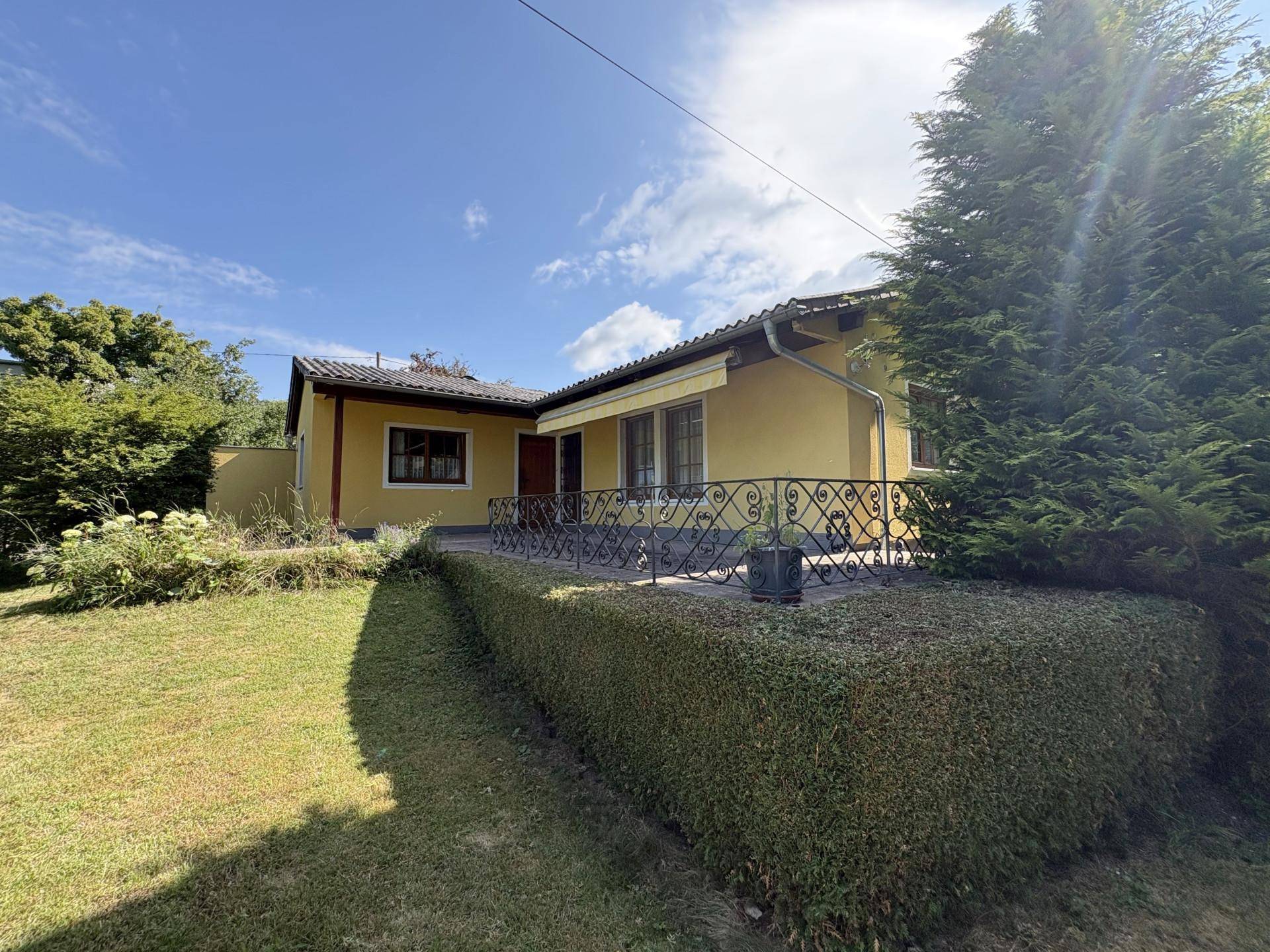 Ansicht des gelben Einfamilienhauses vom Garten aus mit Terrasse und schmiedeeisernem Geländer.