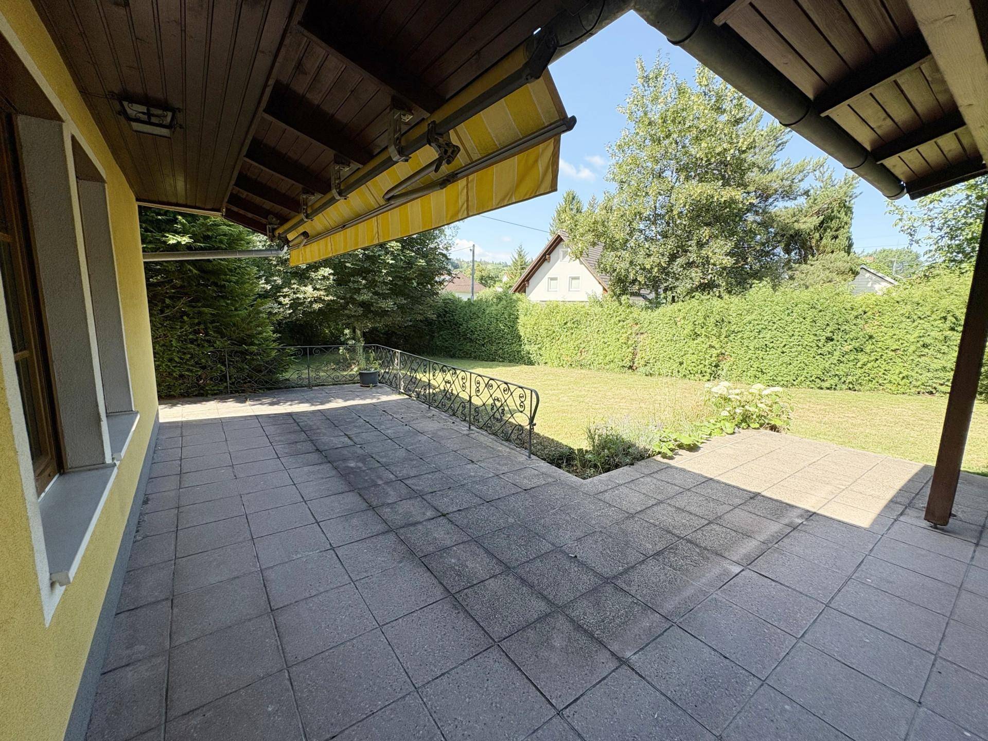 Große gepflasterte Terrasse mit Markise und Blick auf den weitläufigen Gartenbereich.