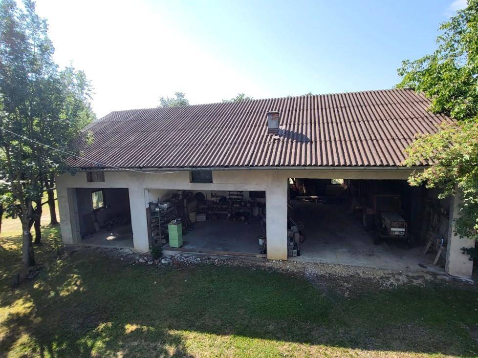 Große Scheune mit mehreren Garagenöffnungen und Ziegeldach, umgeben von Bäumen.