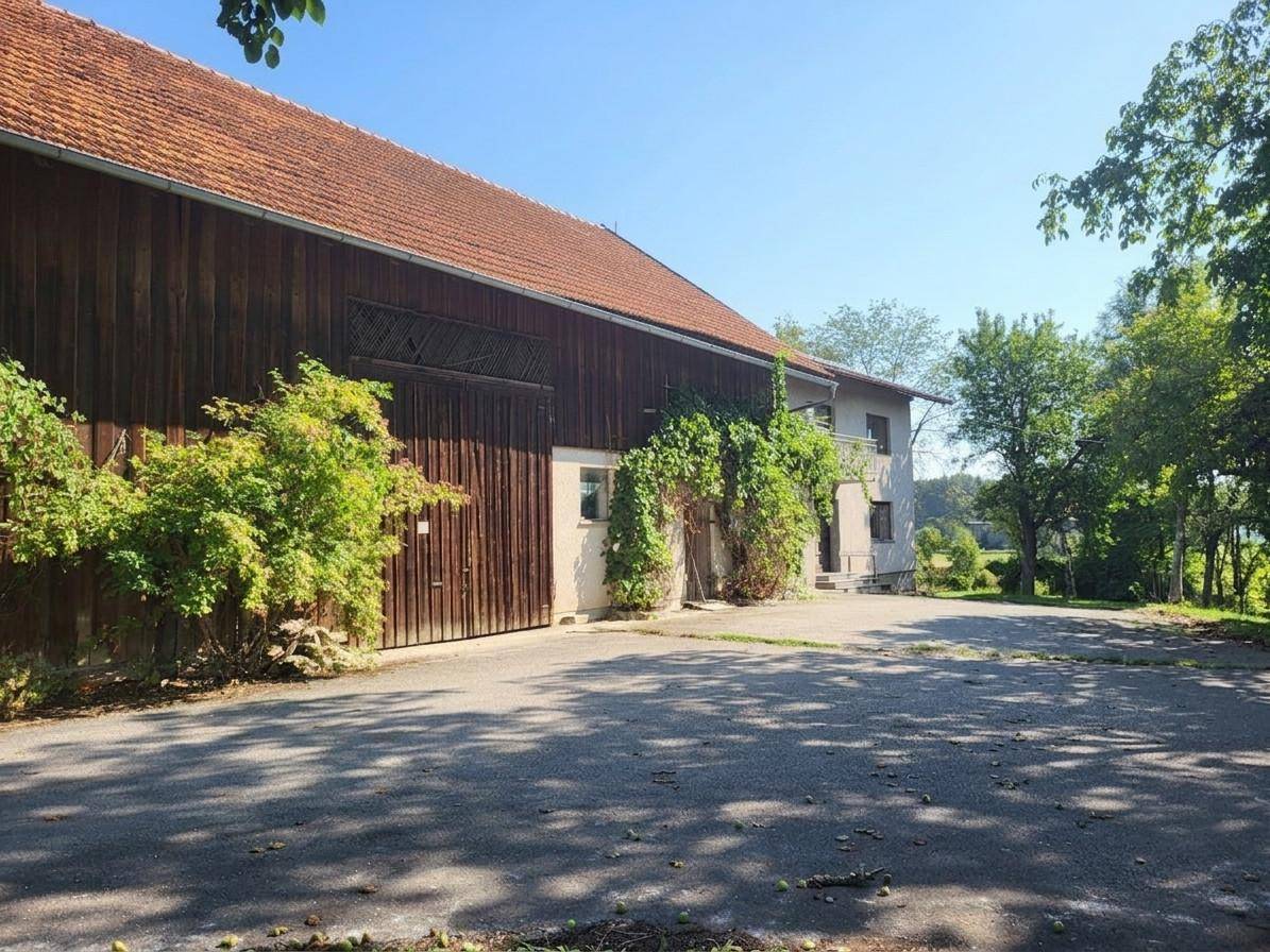 Große Scheune mit Holztoren und begrünten Wänden neben einem Wohngebäude.
