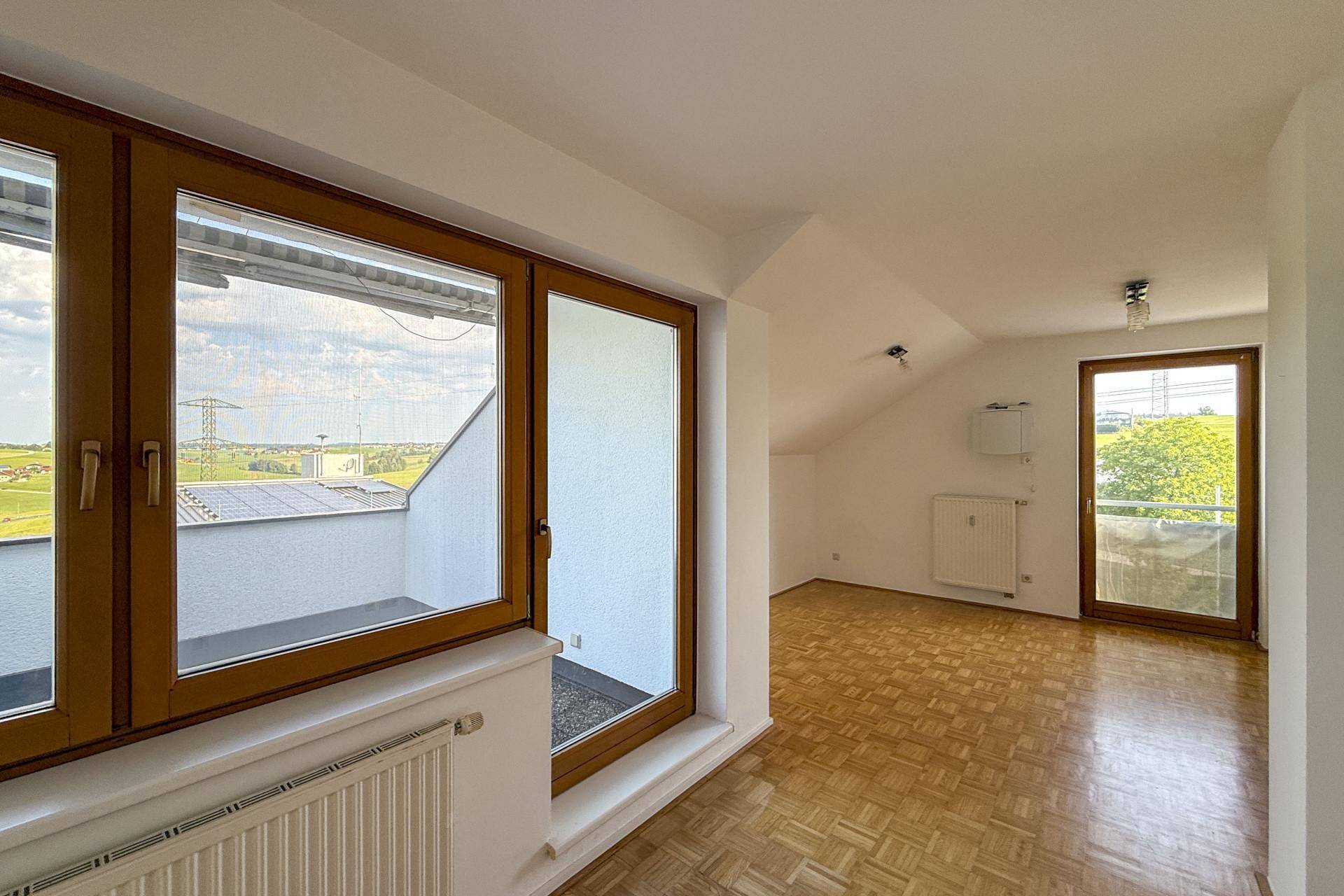 Helles Zimmer mit Parkettboden, Dachschrägen und Zugang zu einem Balkon mit Weitblick.