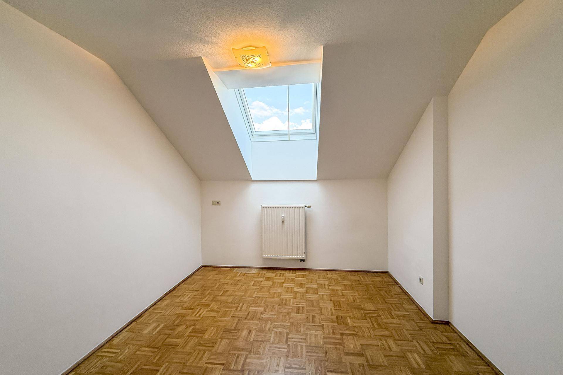 Heller Raum mit Parkettboden, Dachschrägen und einem großen Dachfenster für viel Tageslicht.