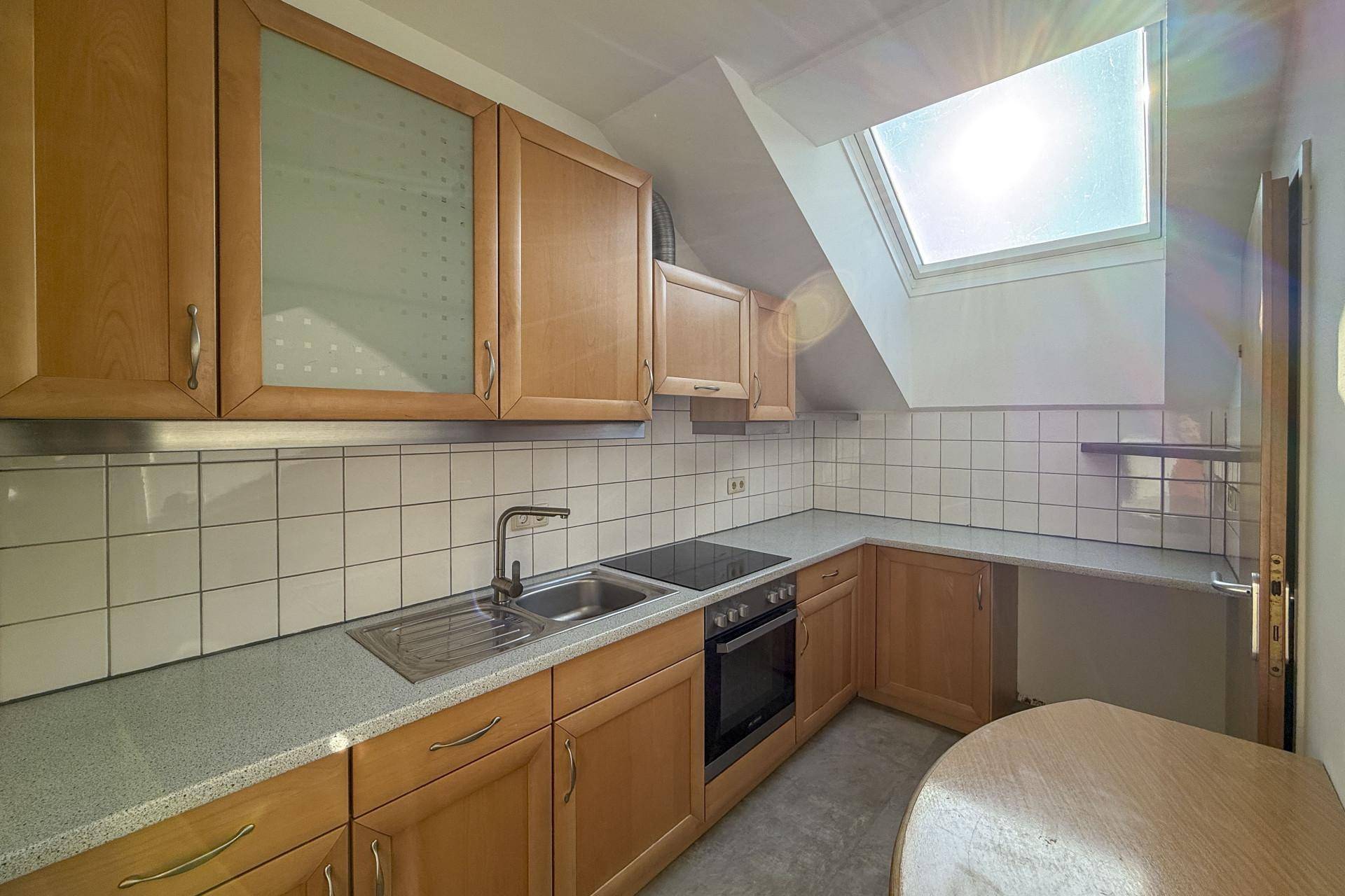 Funktionale Küche mit Holzschränken, weißem Fliesenspiegel und einem Dachfenster für Tageslicht.