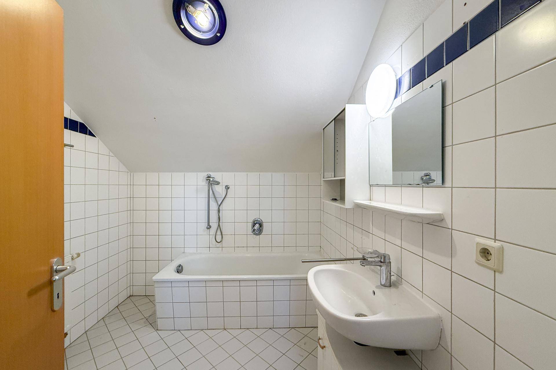 Gefliestes Badezimmer mit Badewanne, Dusche, Einzelwaschbecken und Dachschräge.