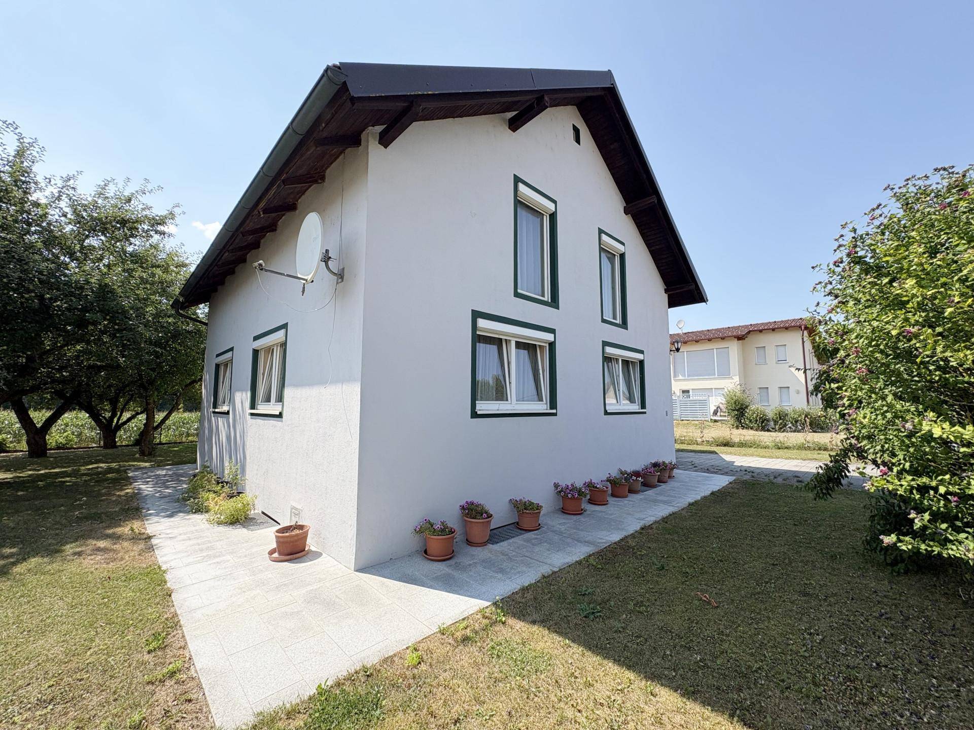 Seitenansicht des Einfamilienhauses mit weißer Fassade, grünen Fensterrahmen und Satellitenschüssel.