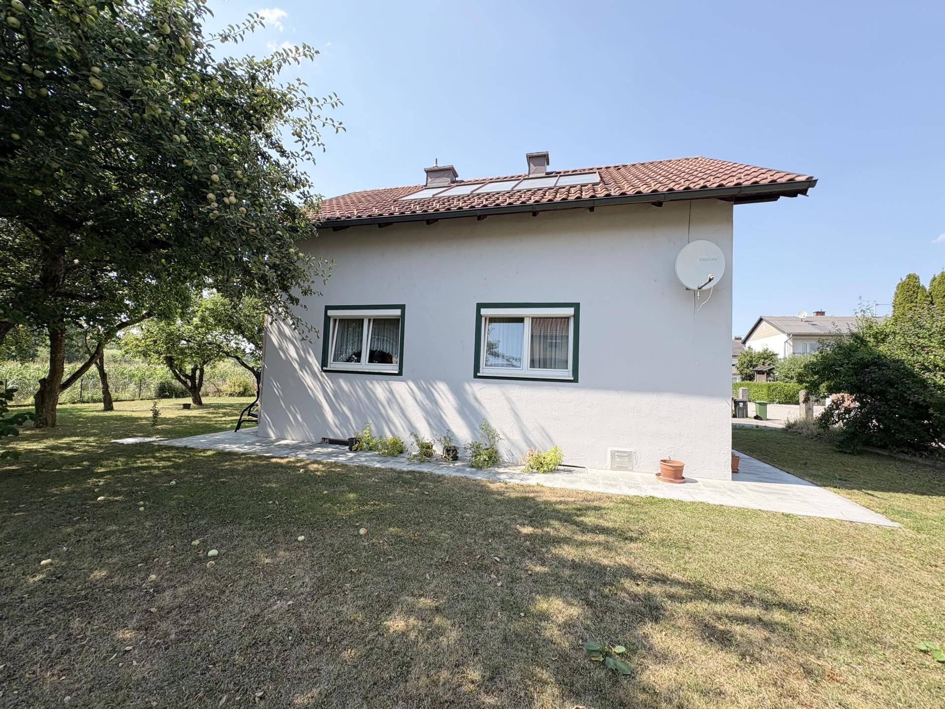 Rückseite des Hauses mit weißer Fassade, Fenstern und großem Garten mit Obstbäumen.
