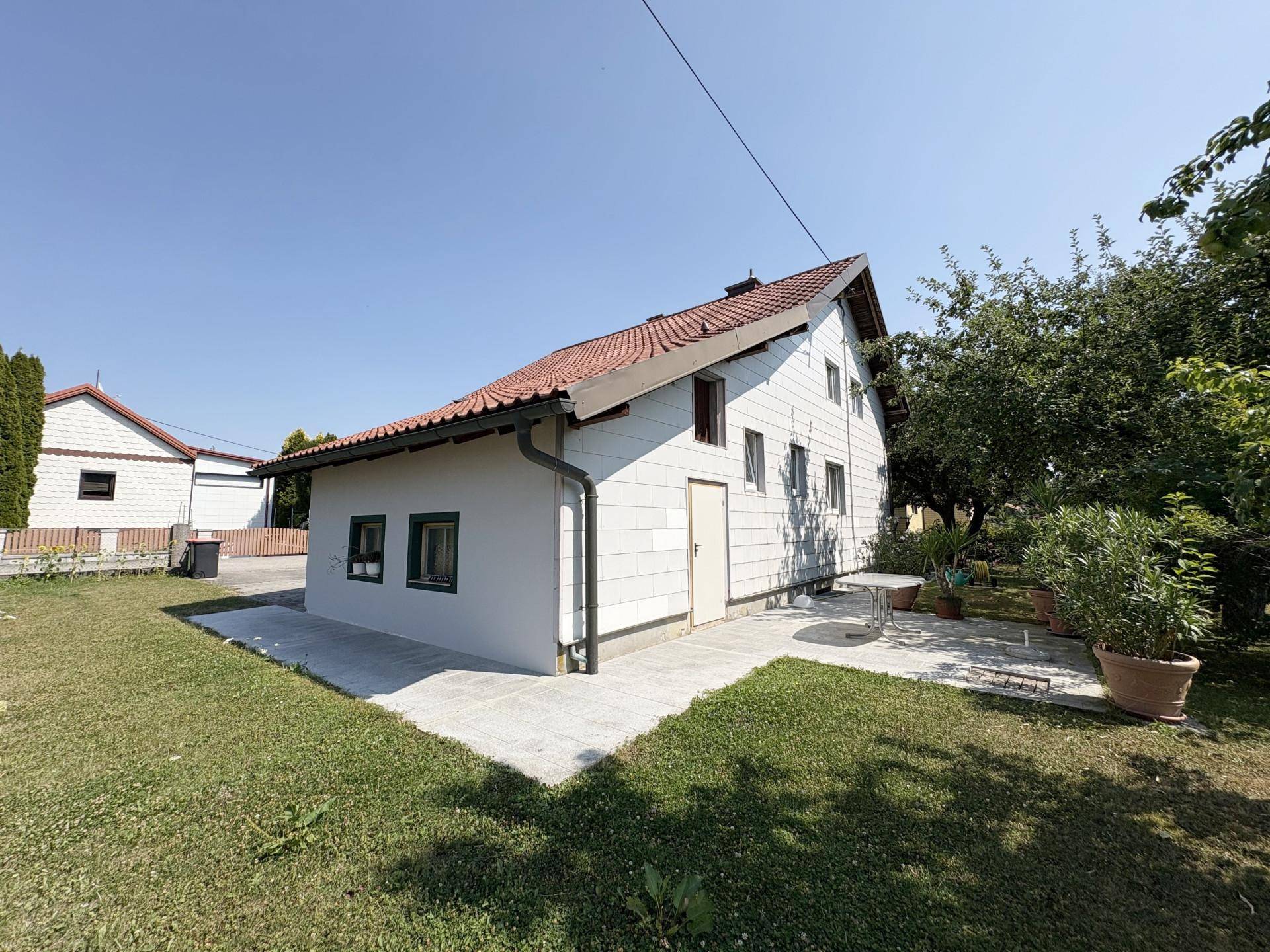 Rückansicht des Hauses mit weißer Fassade, Terrasse und großem Garten mit Bäumen.