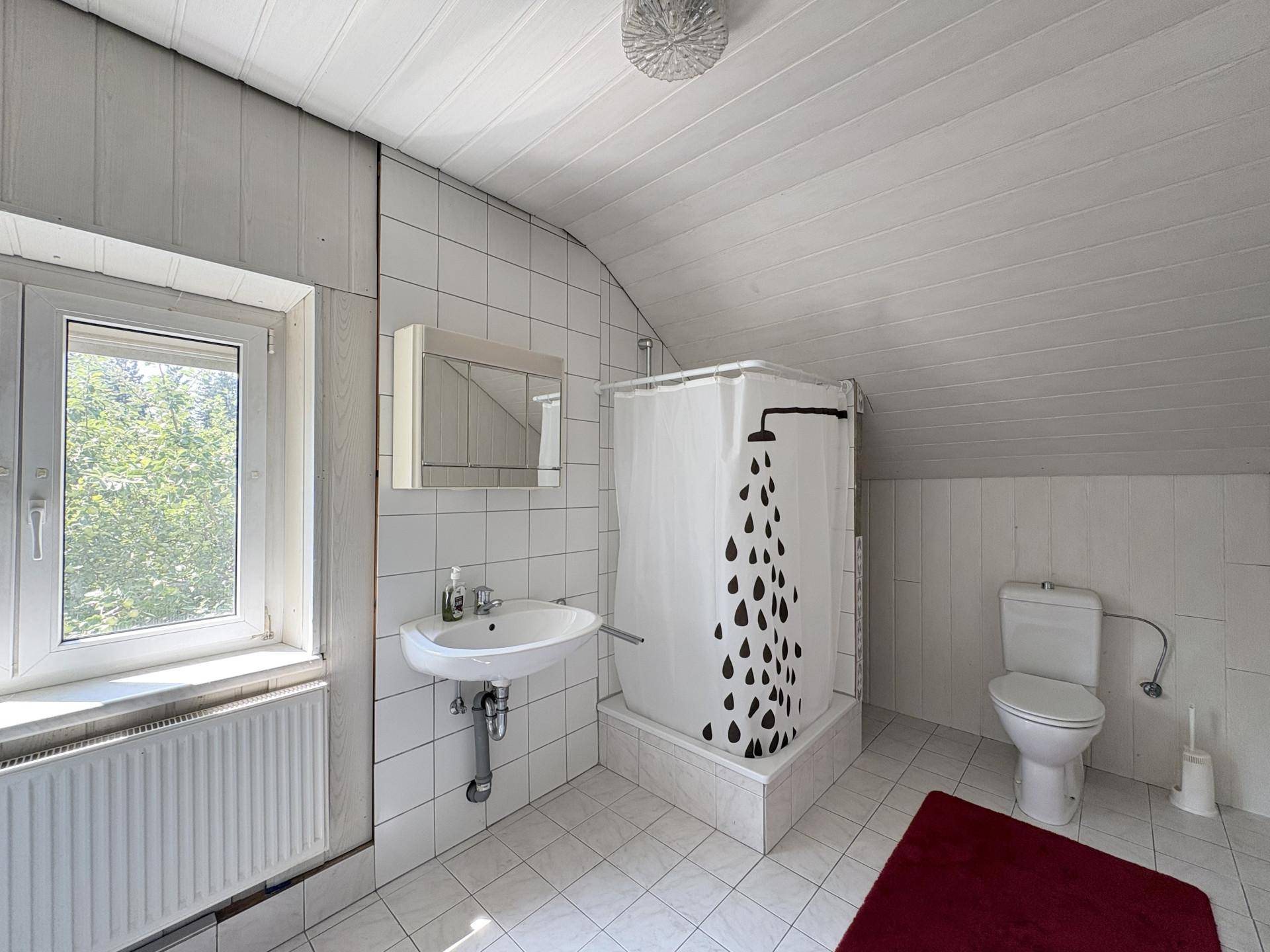 Badezimmer im Dachgeschoss mit Dusche, WC, Waschbecken und weißen Fliesen.