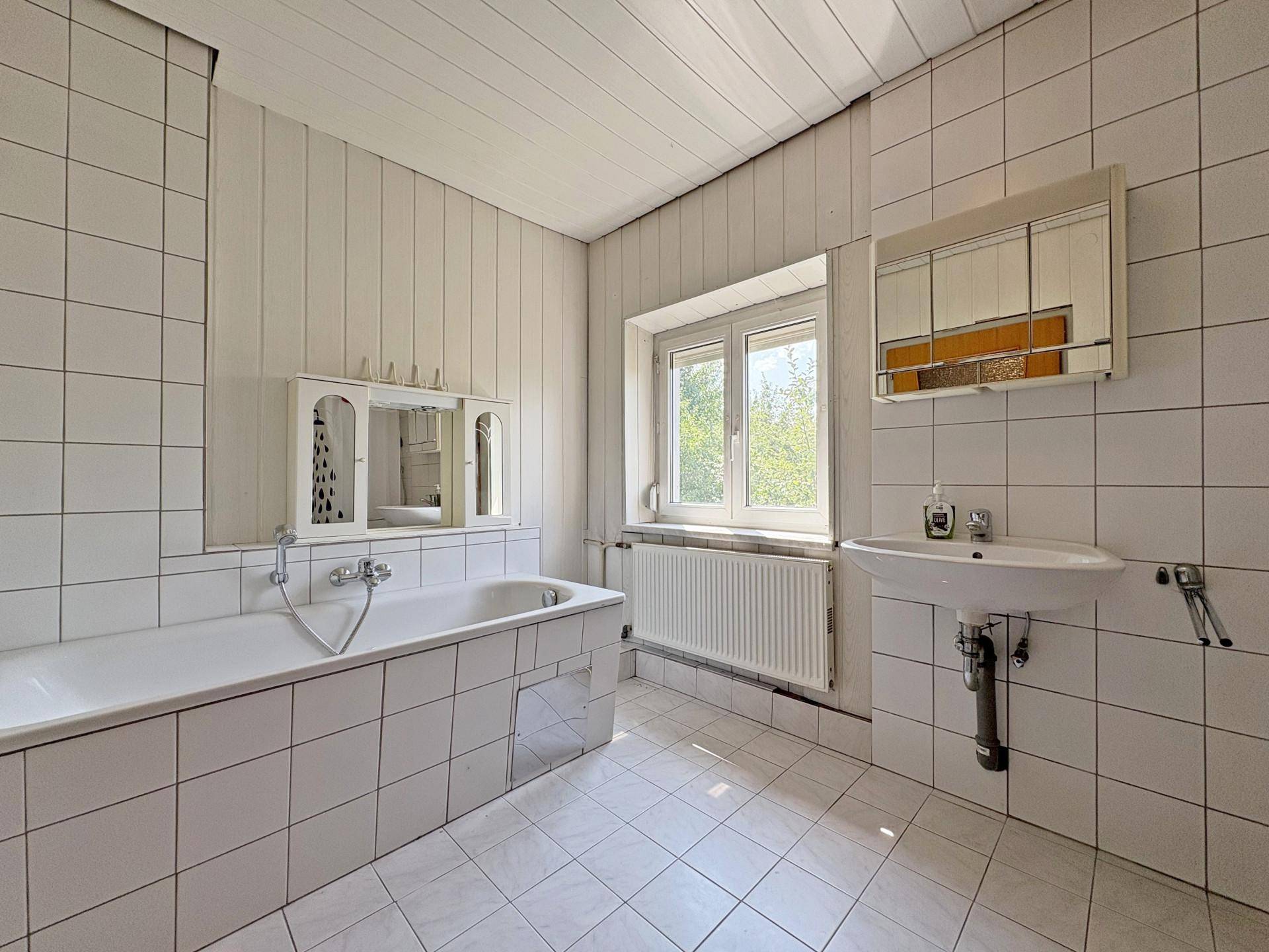 Helles Badezimmer im Dachgeschoss mit Badewanne, Waschbecken und weißen Fliesen.