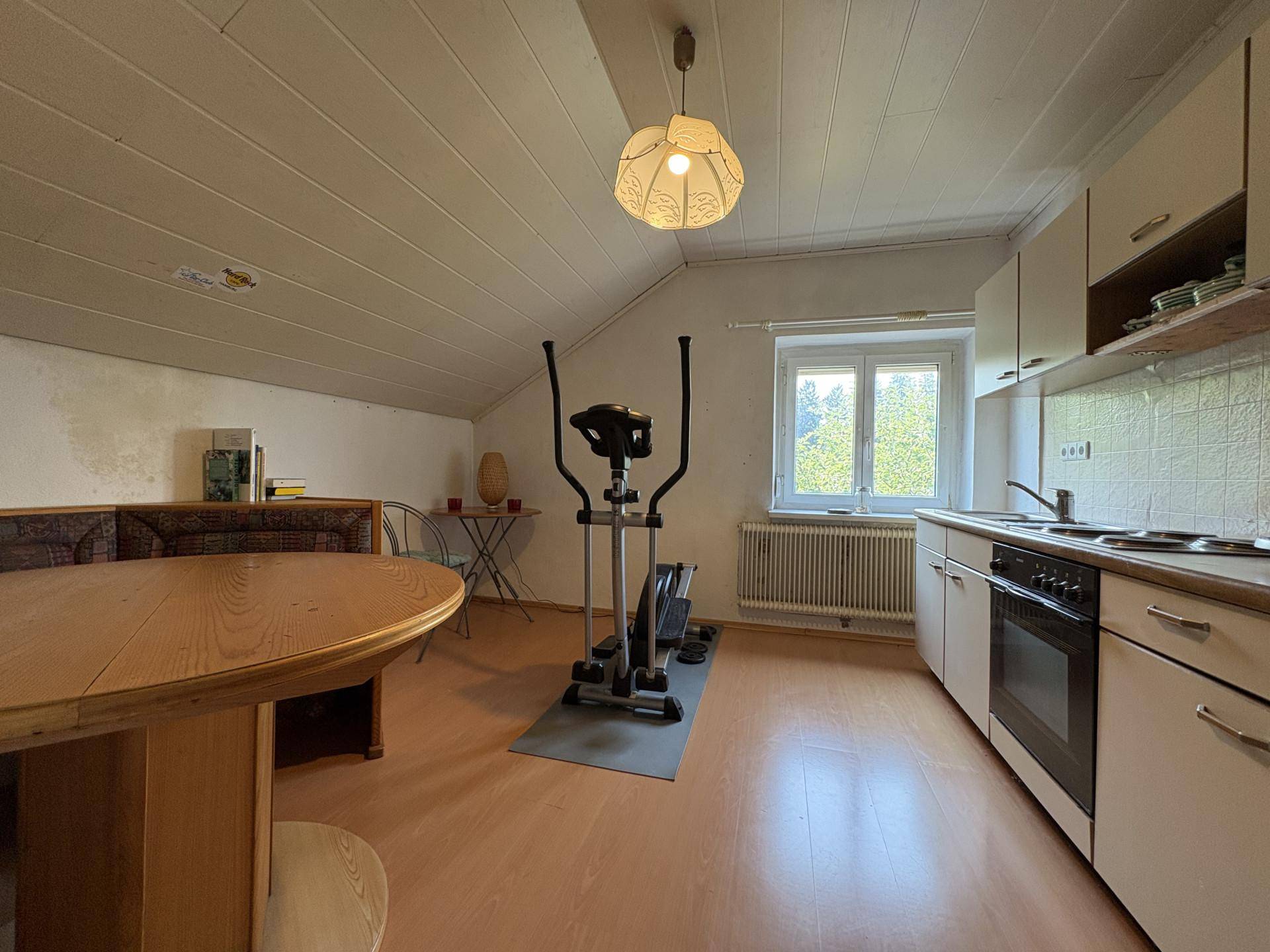 Dachgeschossraum mit kleiner Küchenzeile, Esstisch und Trainingsgerät unter schräger Decke.