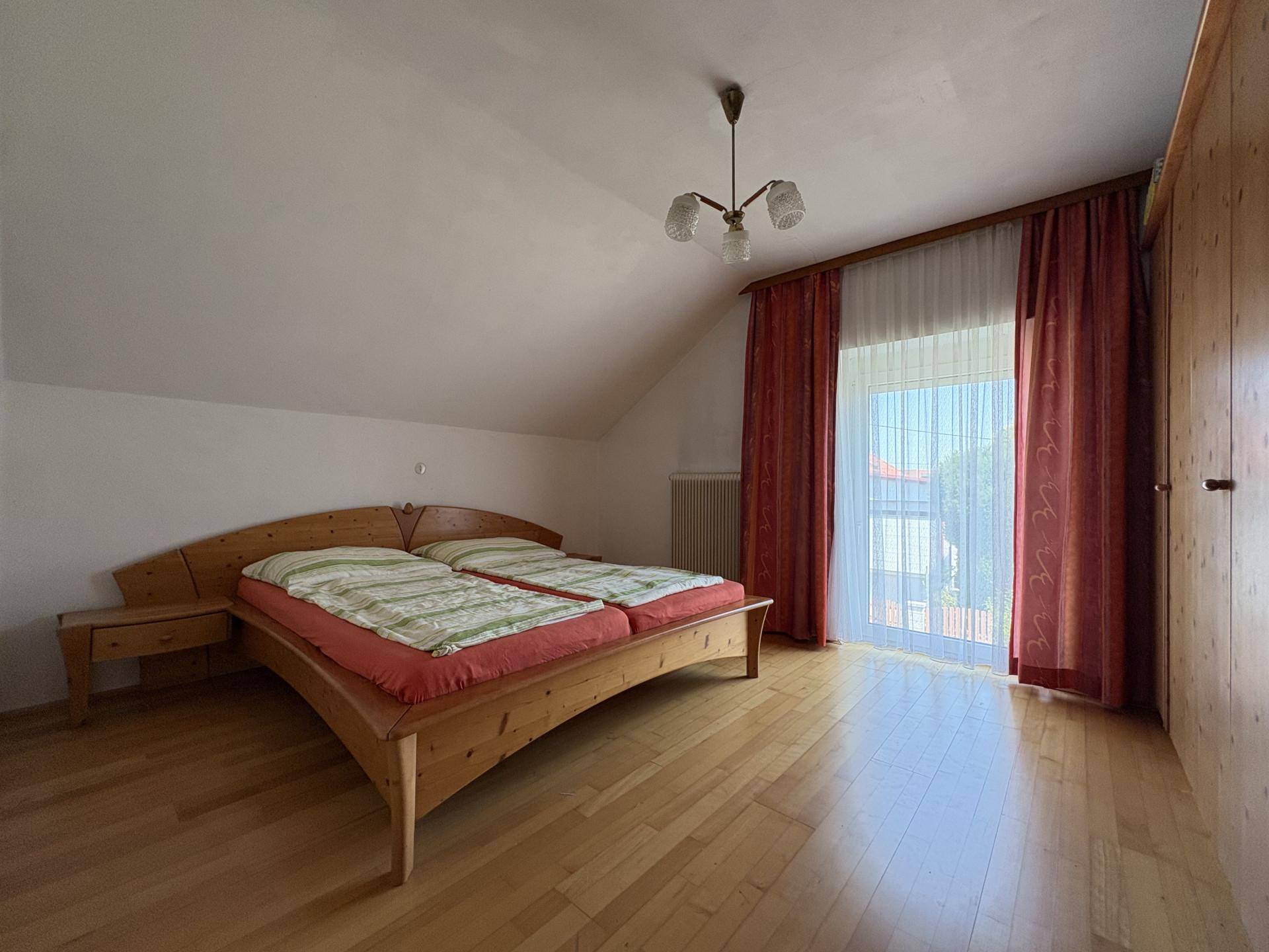 Schlafzimmer im Dachgeschoss mit Holzbett, Kleiderschrank und Zugang zum Balkon.