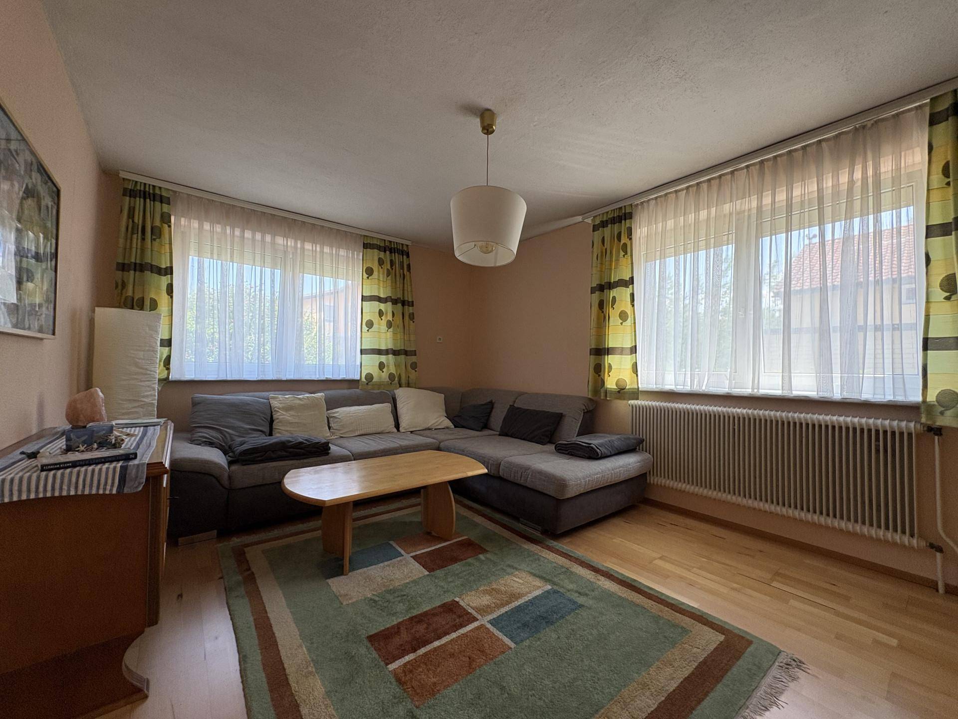 Geräumiges Wohnzimmer mit Ecksofa, Holzboden und großen Fenstern für viel Tageslicht.