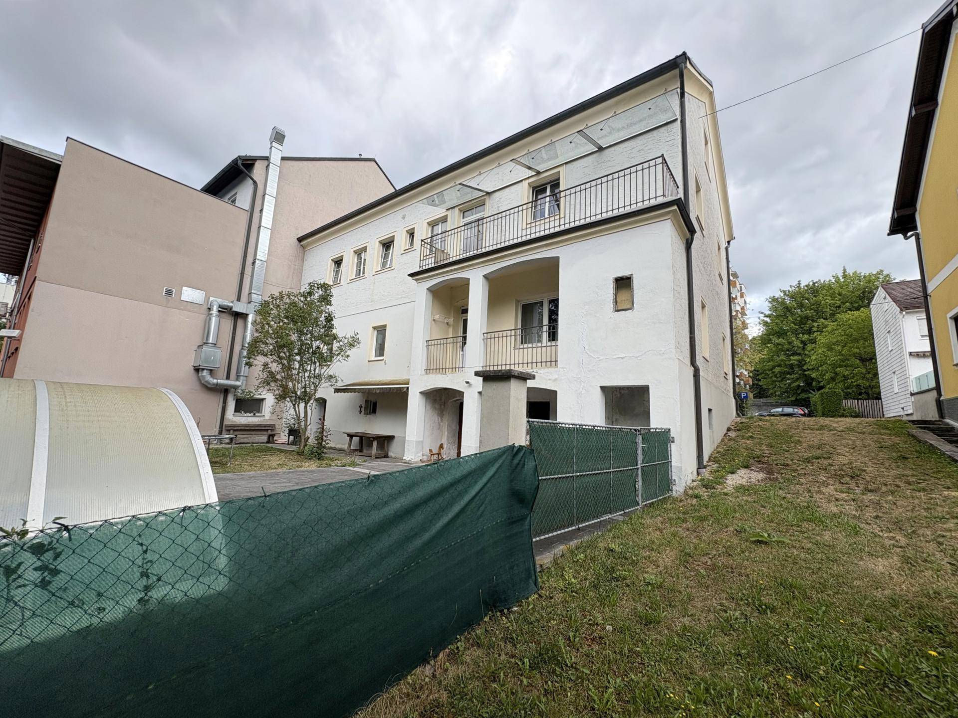 Rückseite des Gebäudes mit mehreren Balkonen und einem leicht abfallenden, begrünten Grundstück.