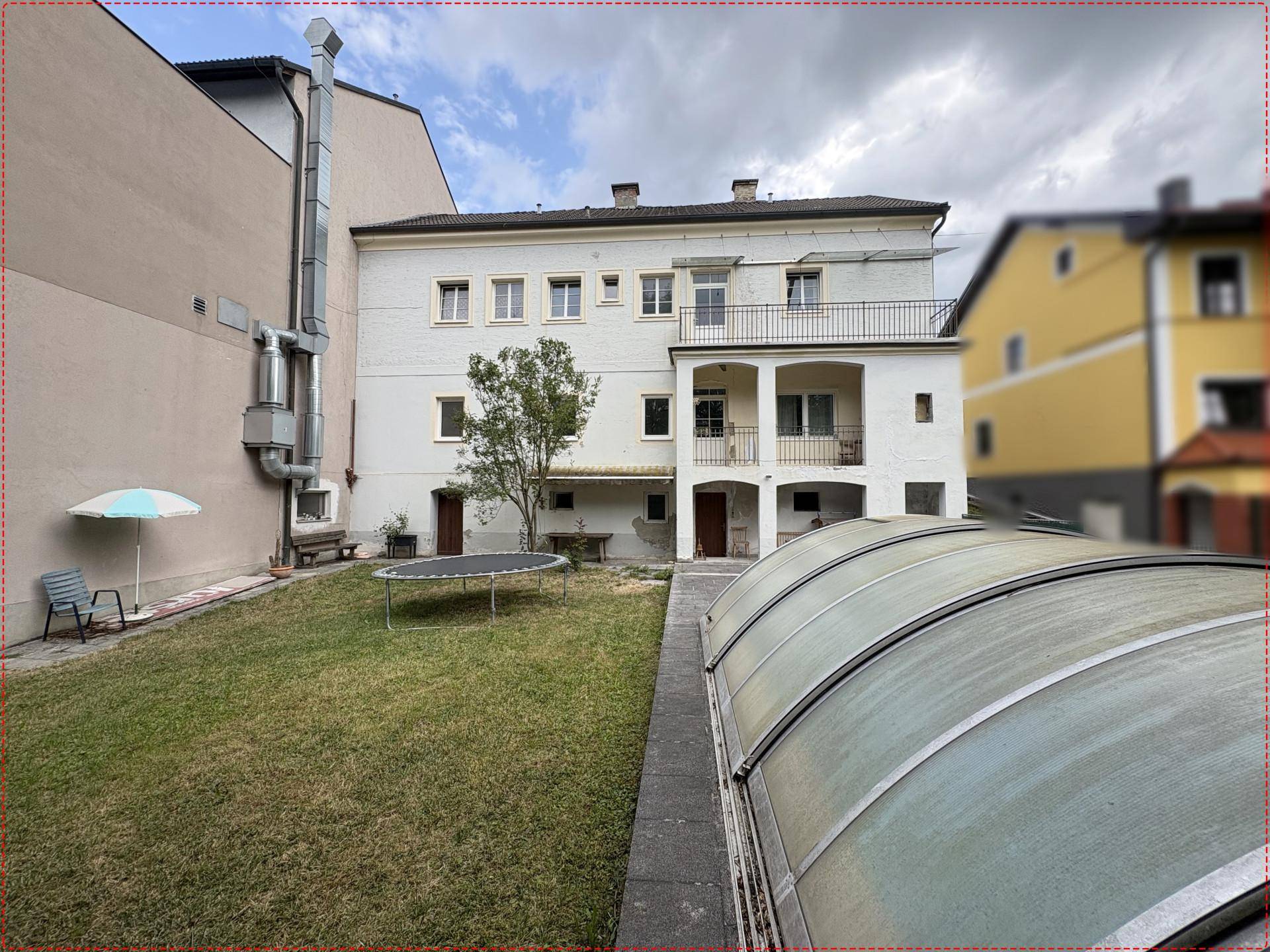 Hinterhof mit Rasenfläche, Trampolin und einer Abdeckung für einen Pool, im Hintergrund das Gebäude.