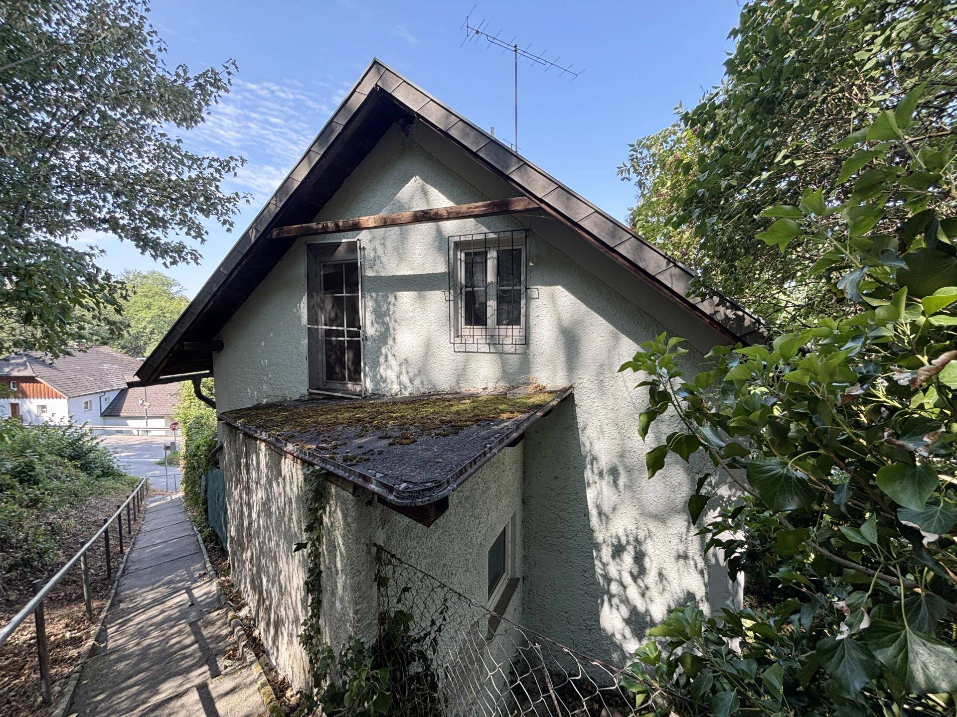 Seitenansicht des Hauses mit Satteldach, vergitterten Fenstern und bewachsenen Wänden.