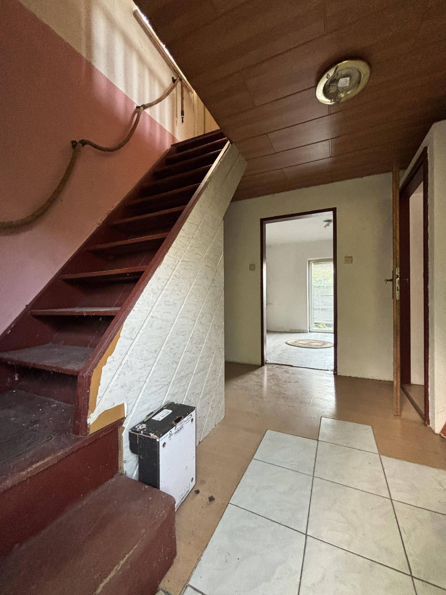 Flur mit Holztreppe und Fliesenboden, der zu weiteren Räumen führt.