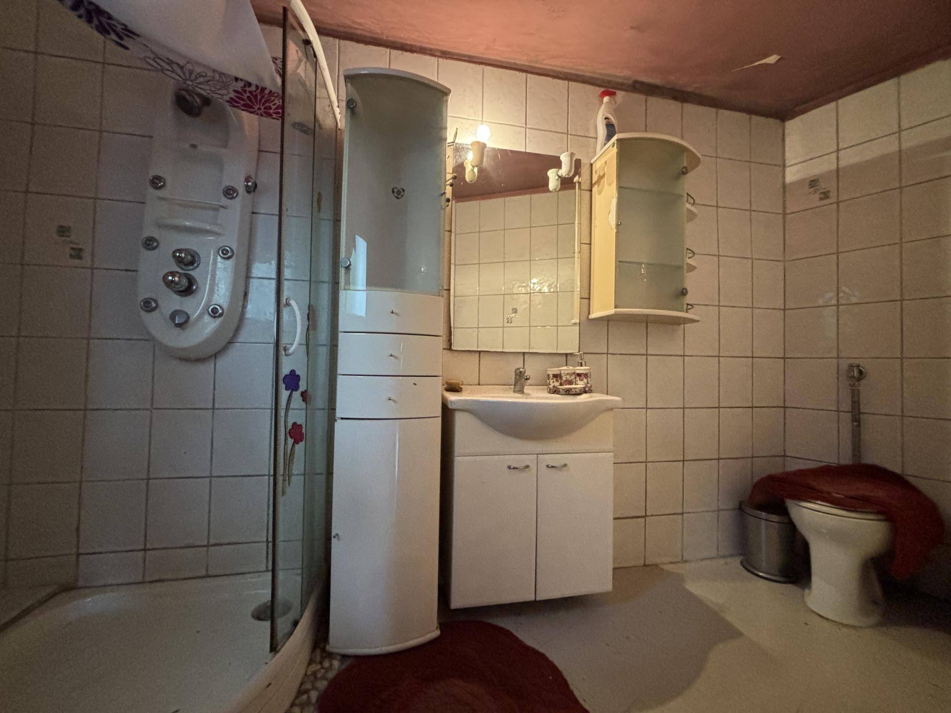 Badezimmer mit Duschkabine, Waschbecken, Spiegel und Toilette in älterem Zustand.