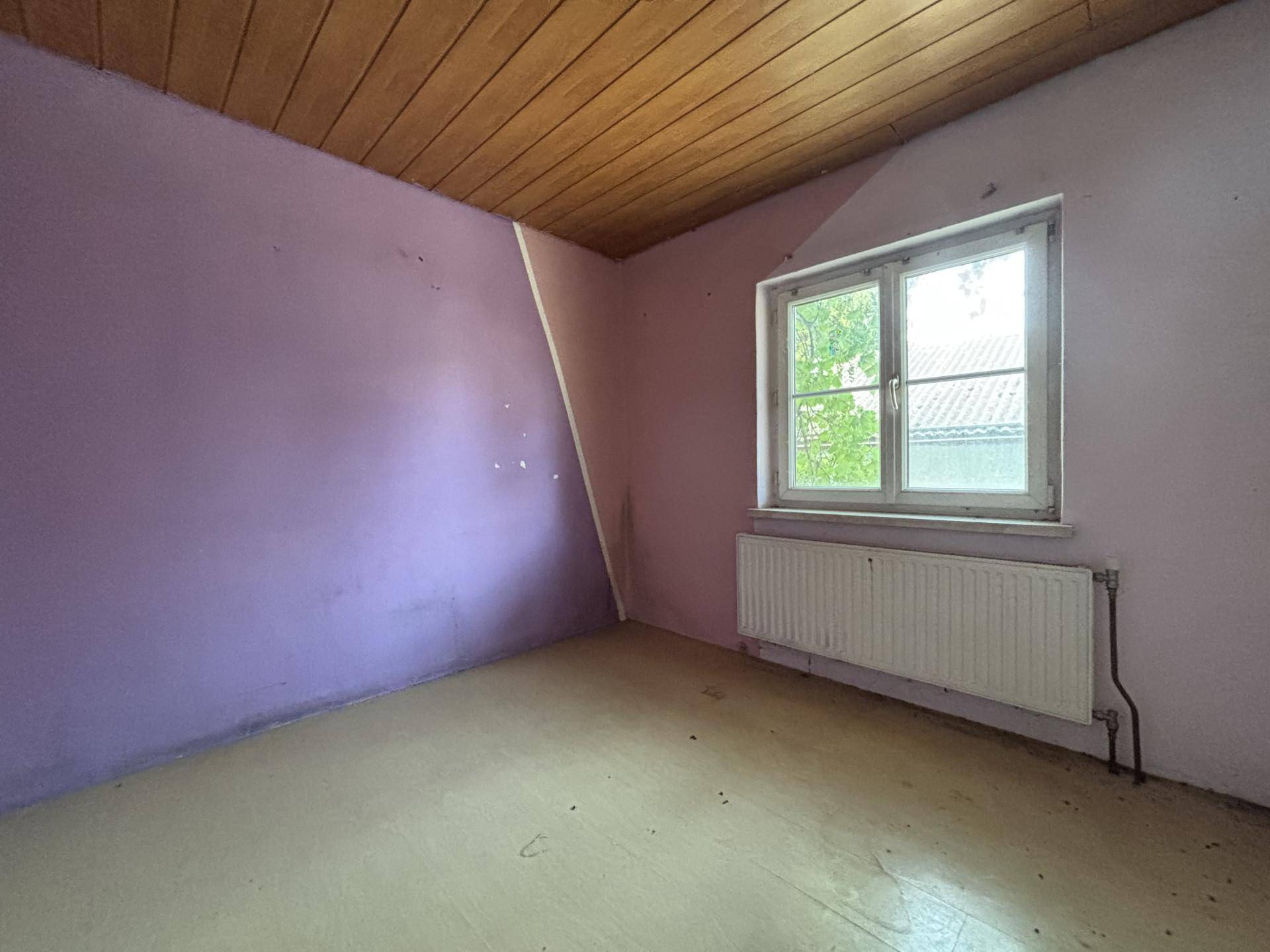 Schlafzimmer mit lila Wänden, Holzdecke, Fenster und Heizkörper, renovierungsbedürftig.