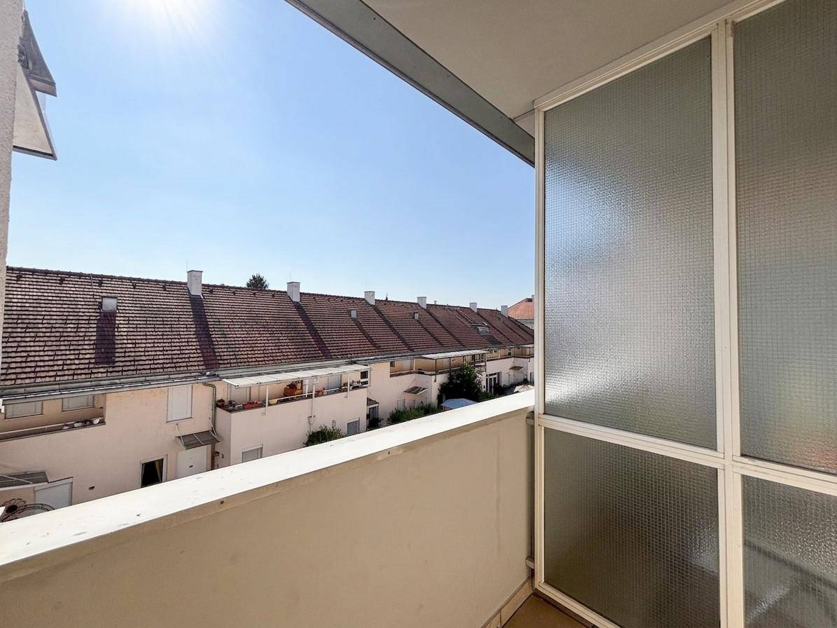 Sonniger Balkon mit Blick auf die Dächer benachbarter Wohnhäuser und klarem Himmel.