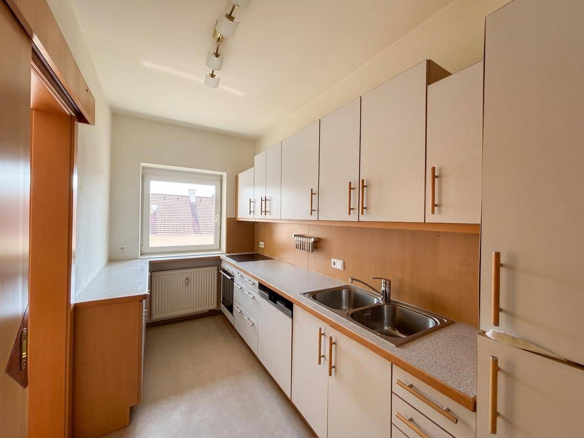 Funktionale Küche mit weißen Schränken, Doppelspüle, Kochfeld und Fenster mit Blick nach draußen.