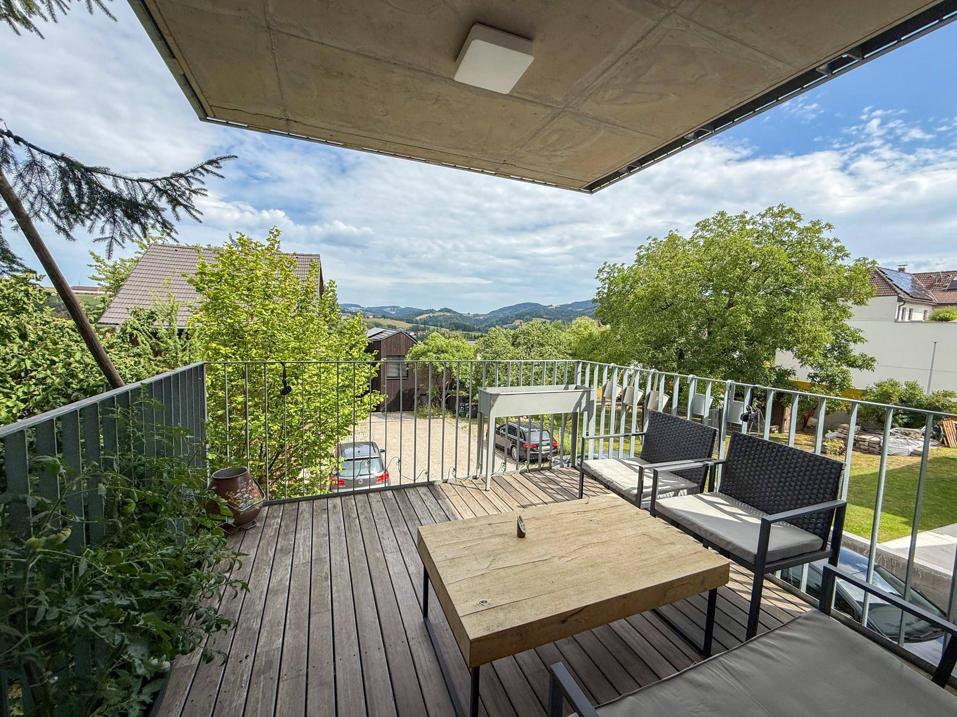 Geräumiger Balkon mit Holzboden, Sitzgelegenheiten und weitem Blick ins Grüne.