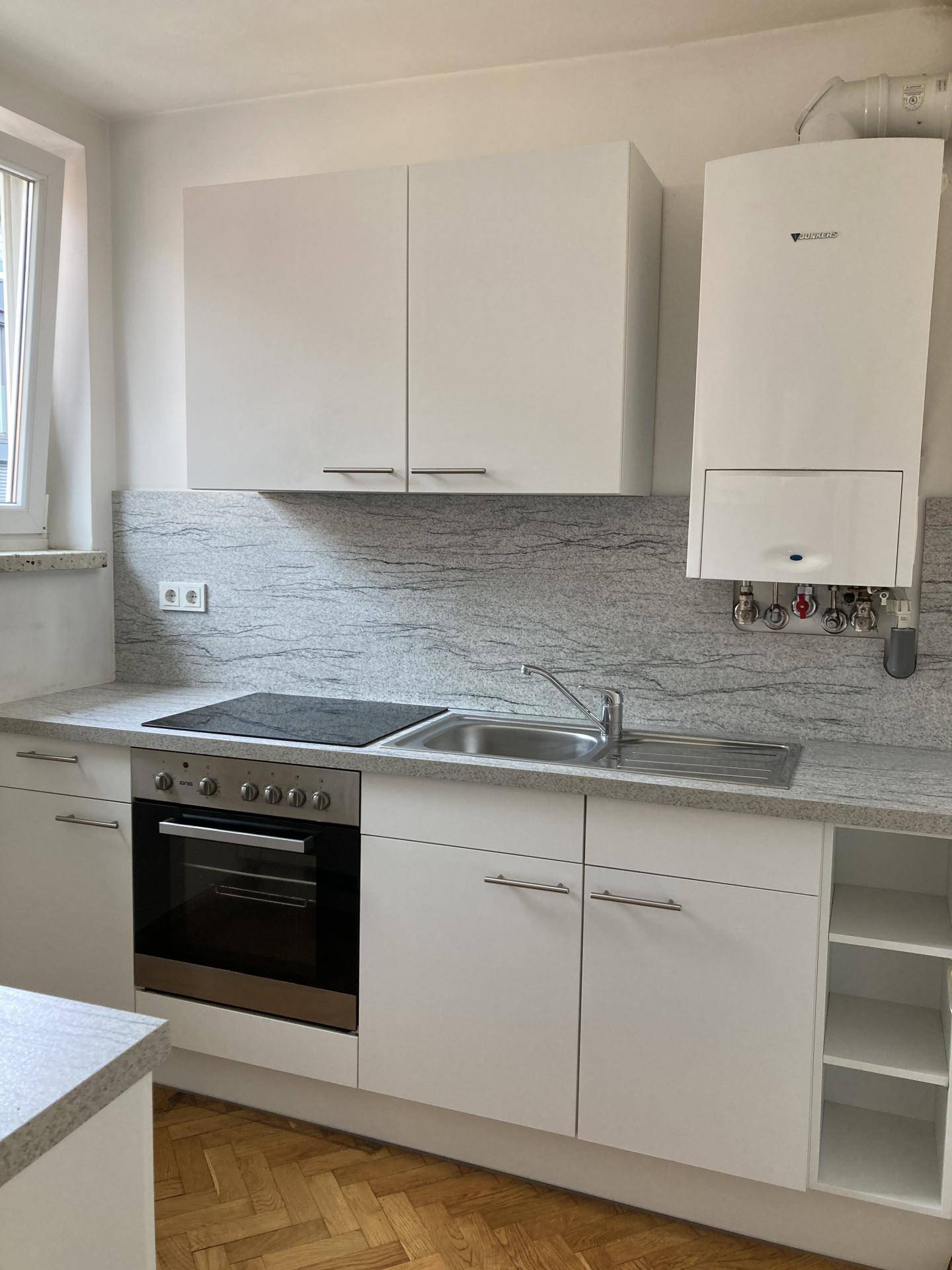 Moderne Einbauküche mit weißen Schränken, heller Stein-Arbeitsplatte und Gastherme.